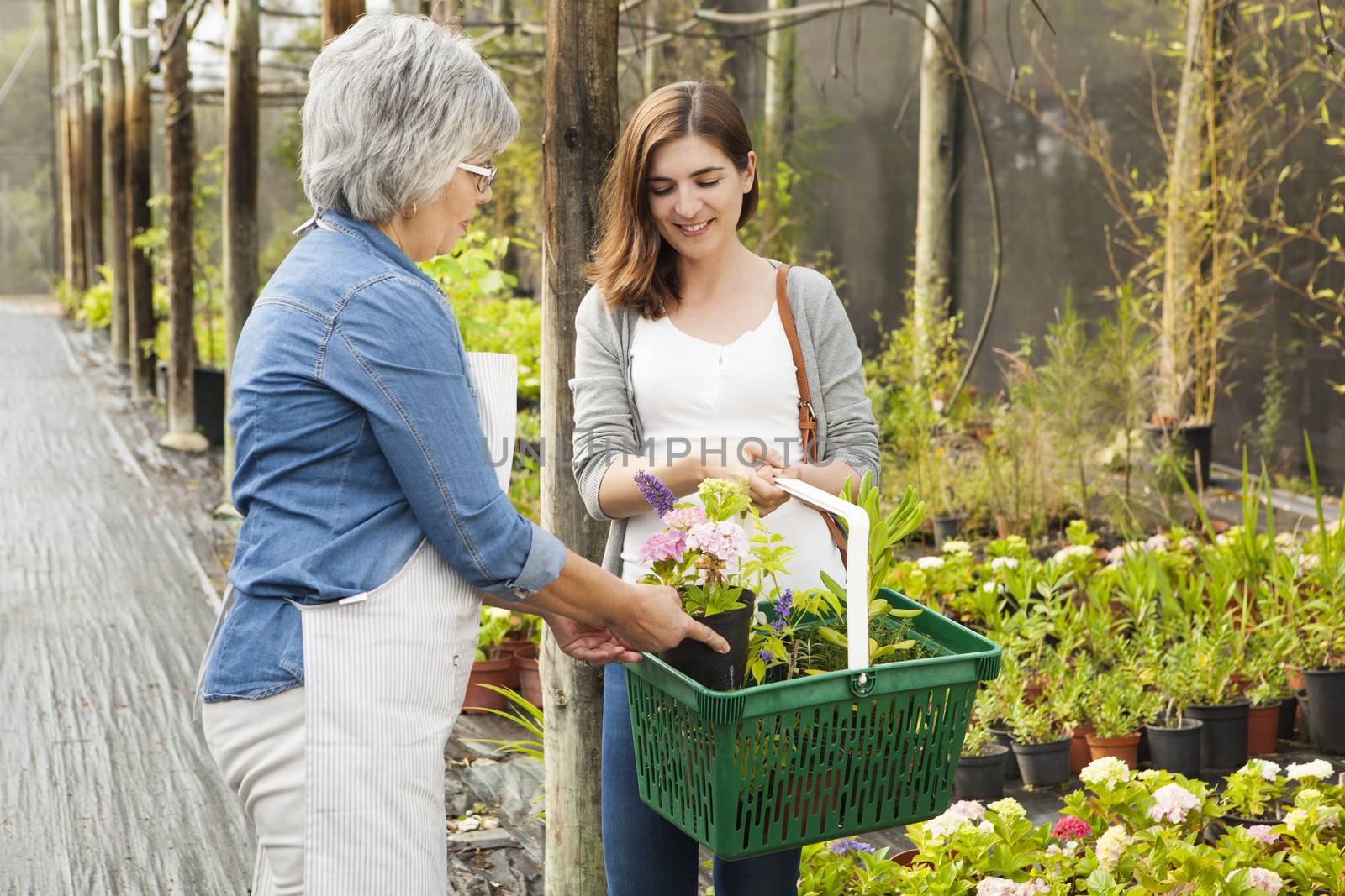 Beautiful mature florist helping a female customer to choose plants