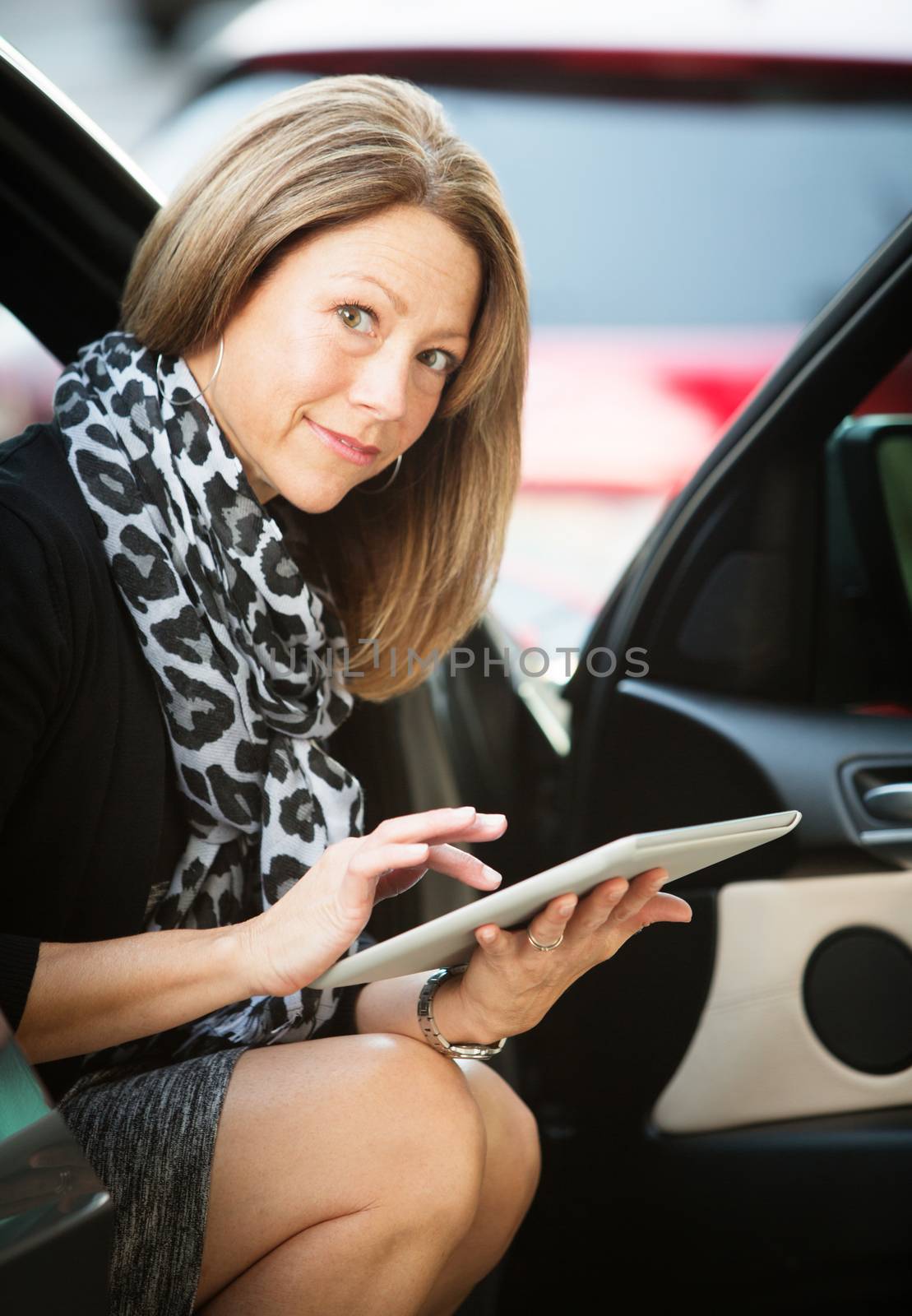 Business woman sitting in her car using a tablet computer