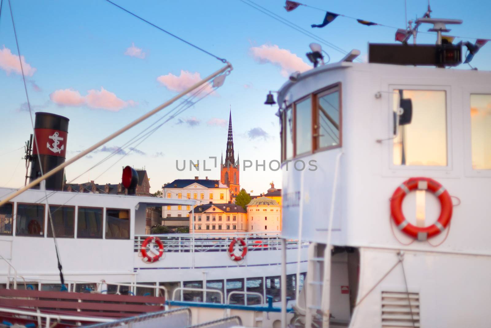 Swedish capital Stockholm in sunset. White traditional wooden  ferry steamer and old medieval downtown of Gamla stan in the background. Focus on background. Horisontal composition.