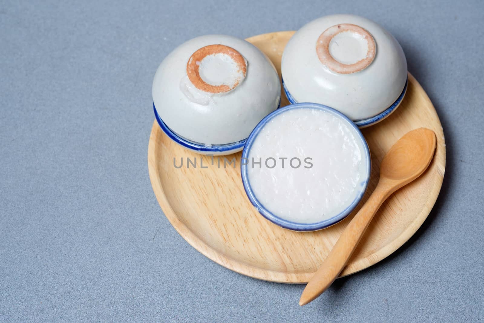 coconut milk custard in small porcelain cup (Thai dessert) in wooden dish on blue table.