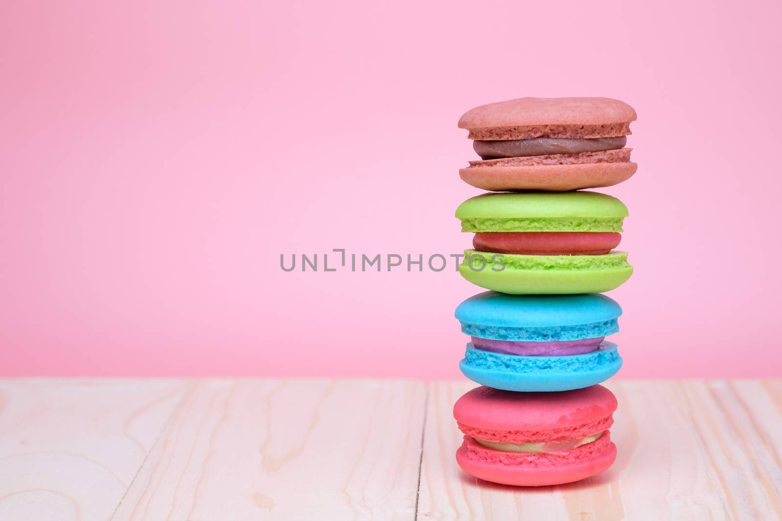 Sweet and colourful french macaroons on wooden table and pastel pink background