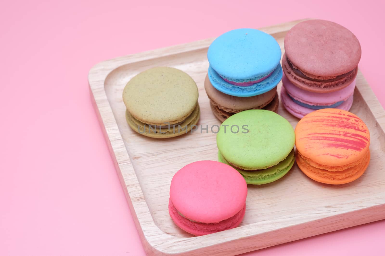 Wooden dish of Sweet and colourful french macaroons on  pastel pink background