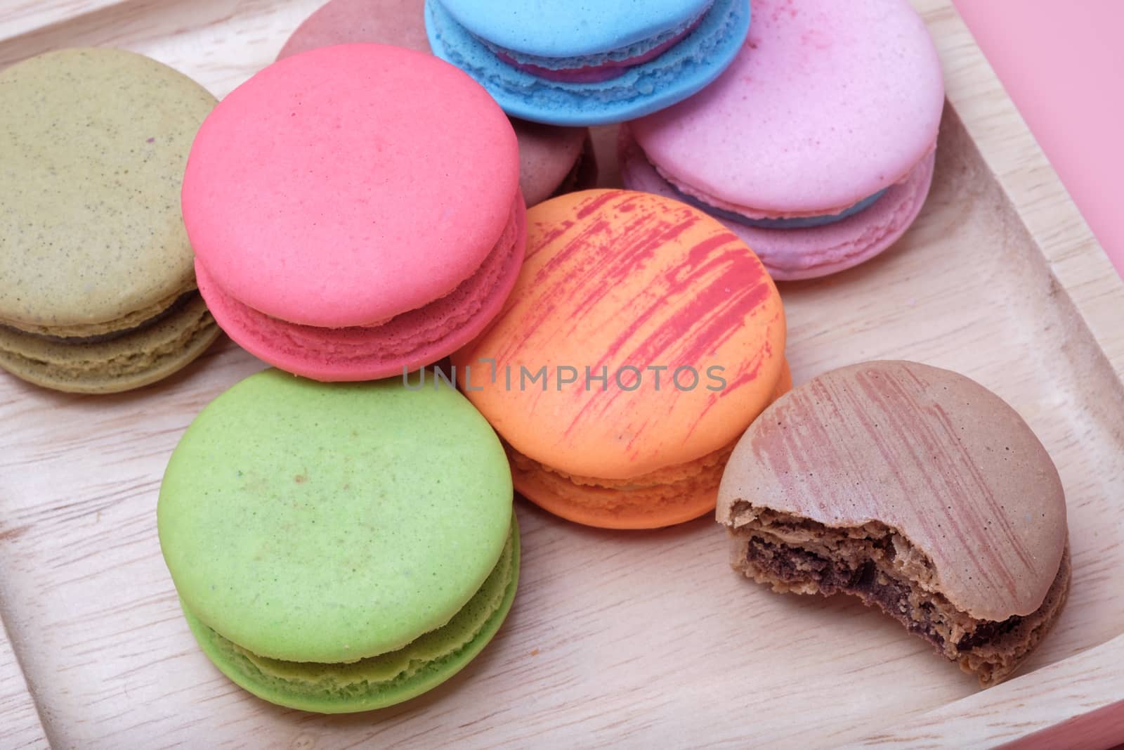 Wooden dish of Sweet and colourful french macaroons on  pastel pink background