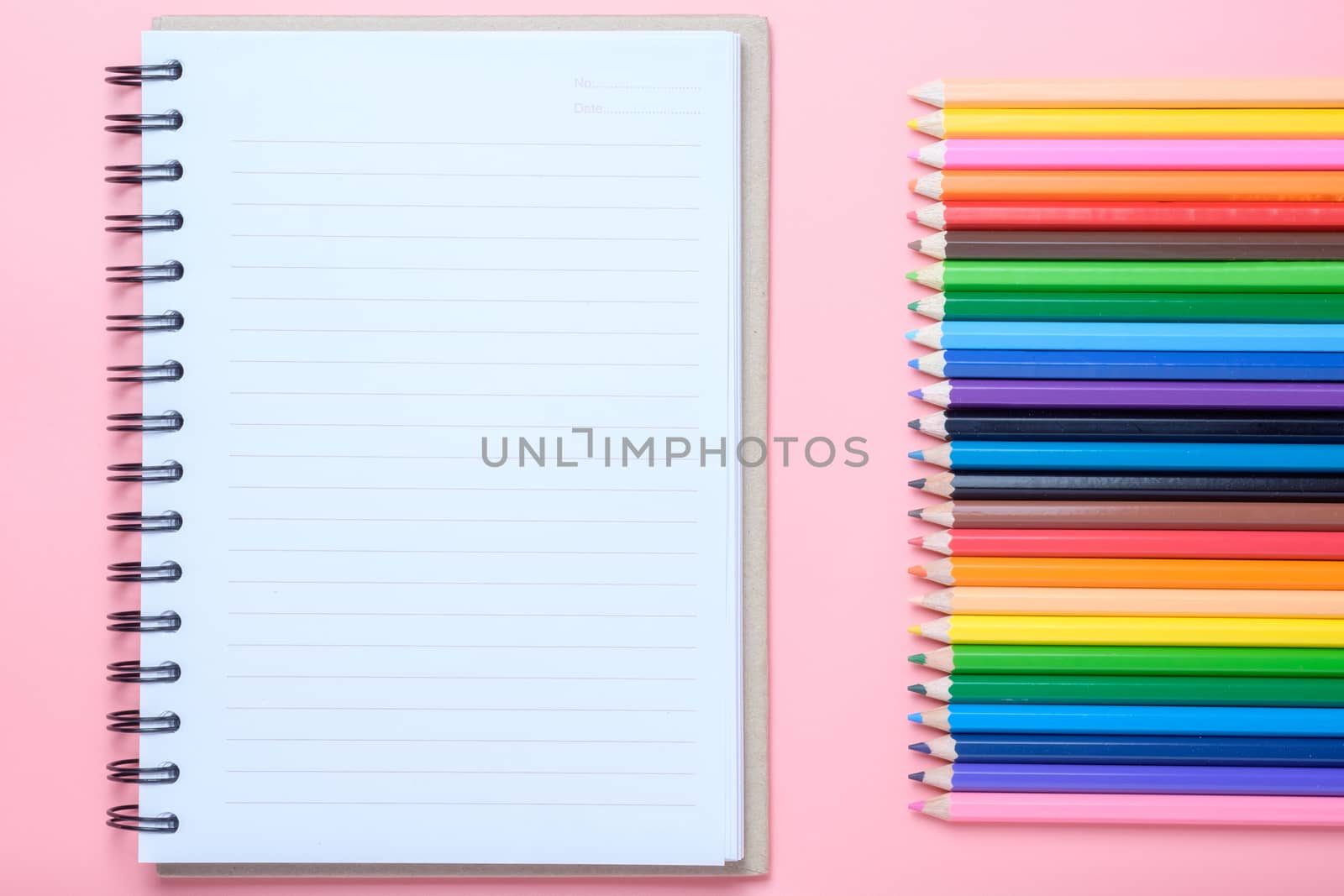 Notebook and colored pencils on pink background.