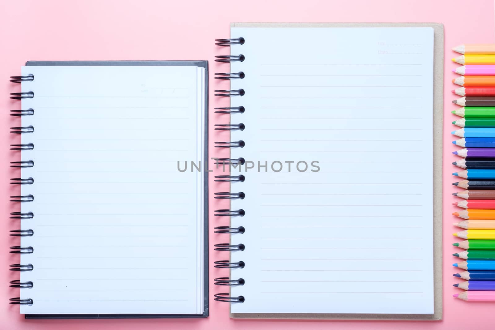 Notebook and colored pencils on pink background.