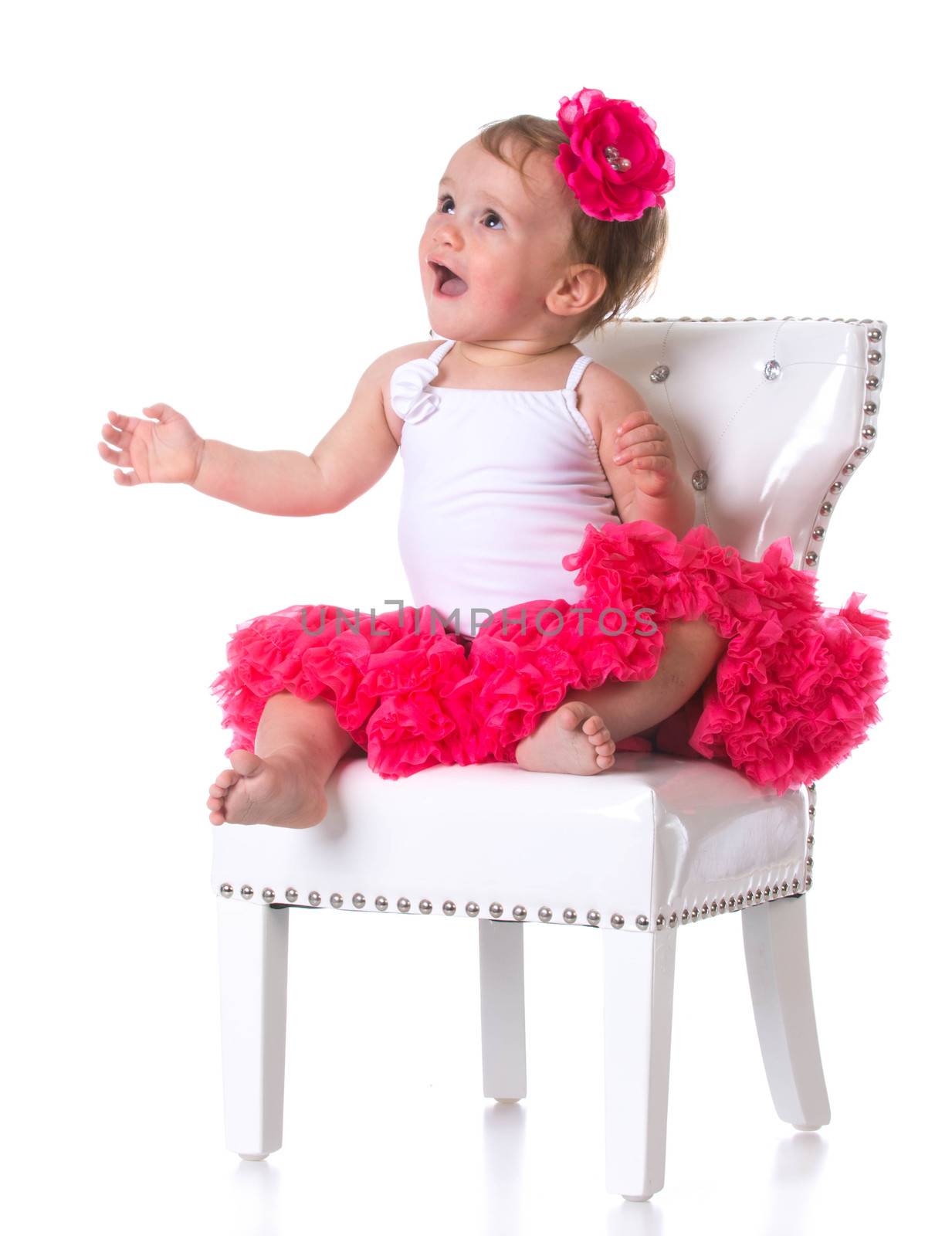 happy one year old girl wearing tutu sitting on a white chair