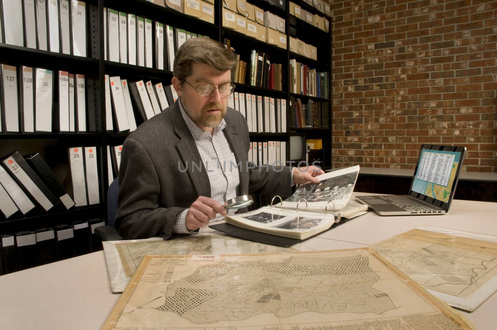 Researcher in archive, searching through maps and photographs. Model released. (All maps and photos shown in archive are public domain. Image on computer was created for this photograph.)