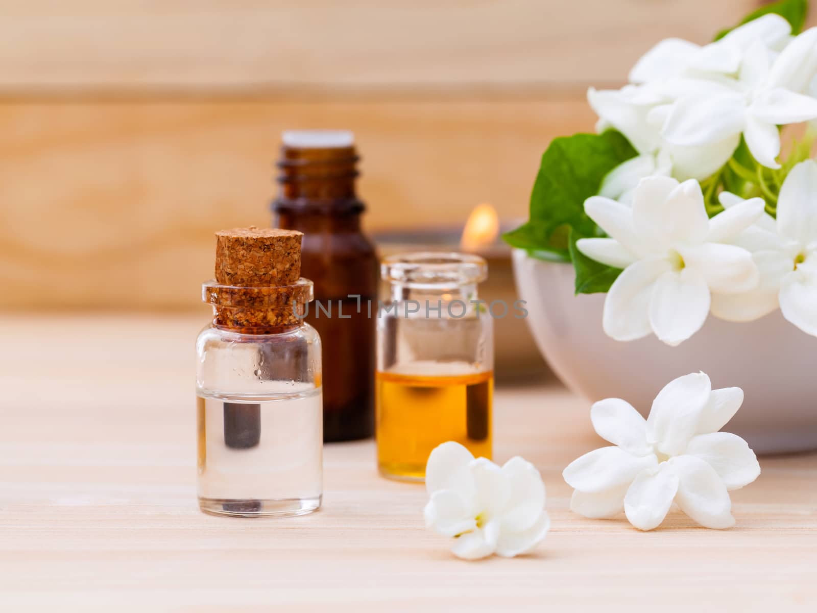 Aroma oil bottles arranged with jasmine flowers on wooden background .