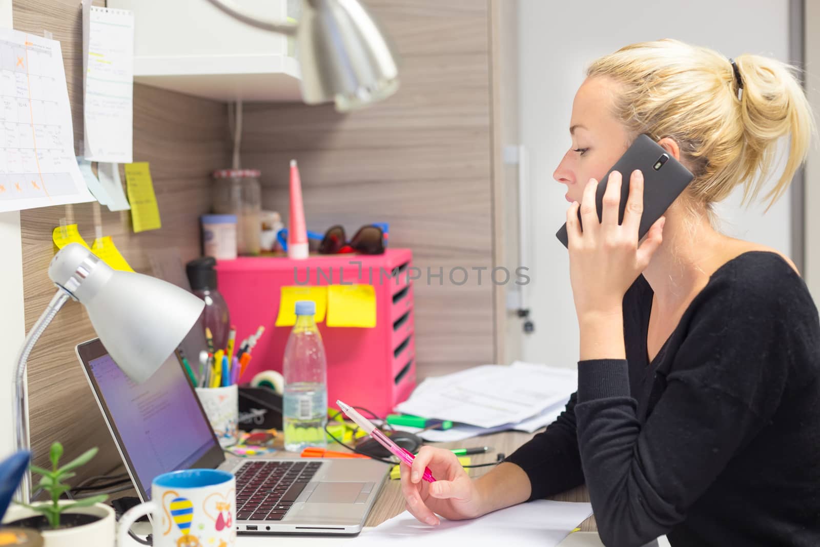 Business and entrepreneurship consept. Beautiful blonde business woman talking on mobile phone in colorful modern creative working environment.