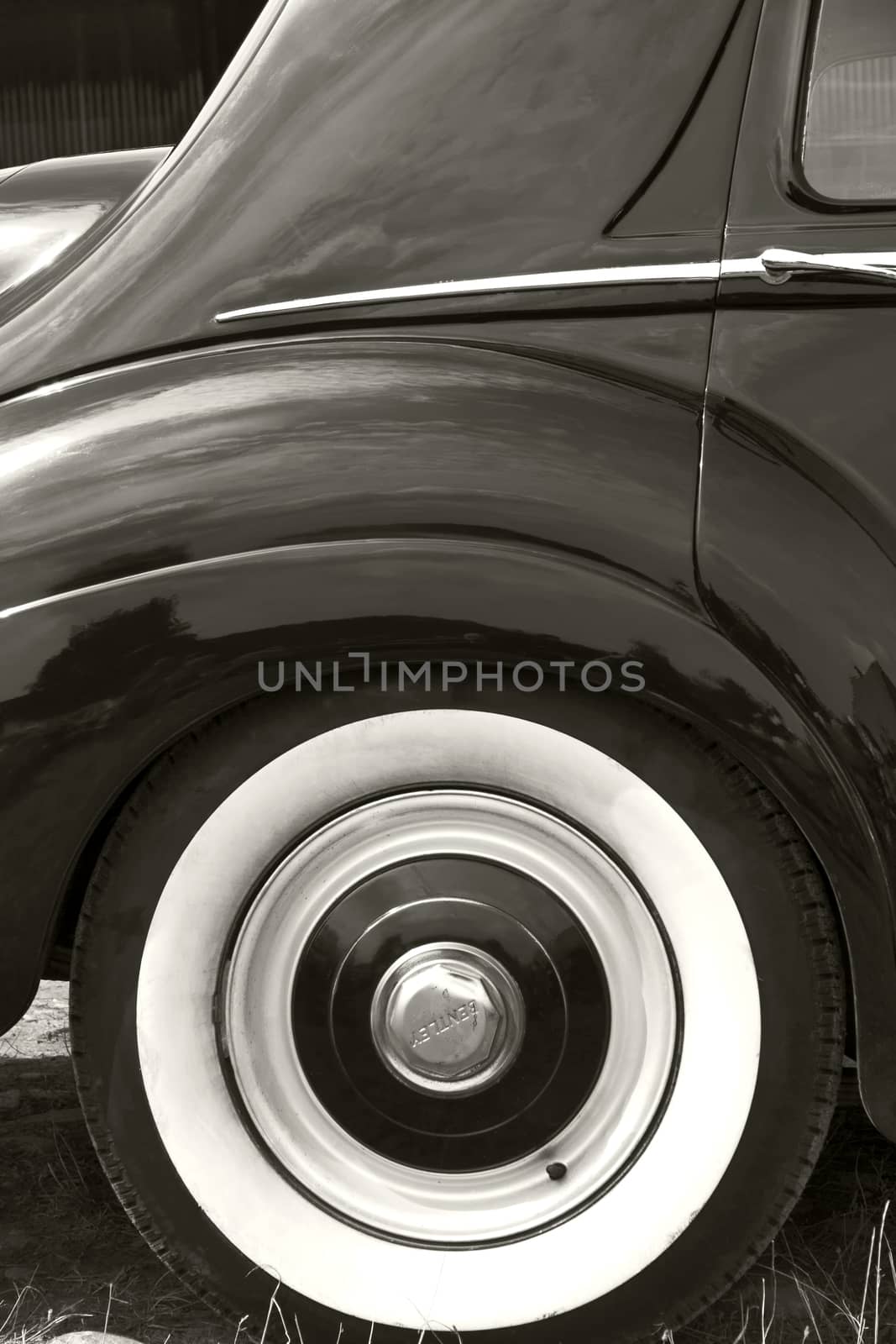 The rear and the rear wheel of a vintage car in black and white.