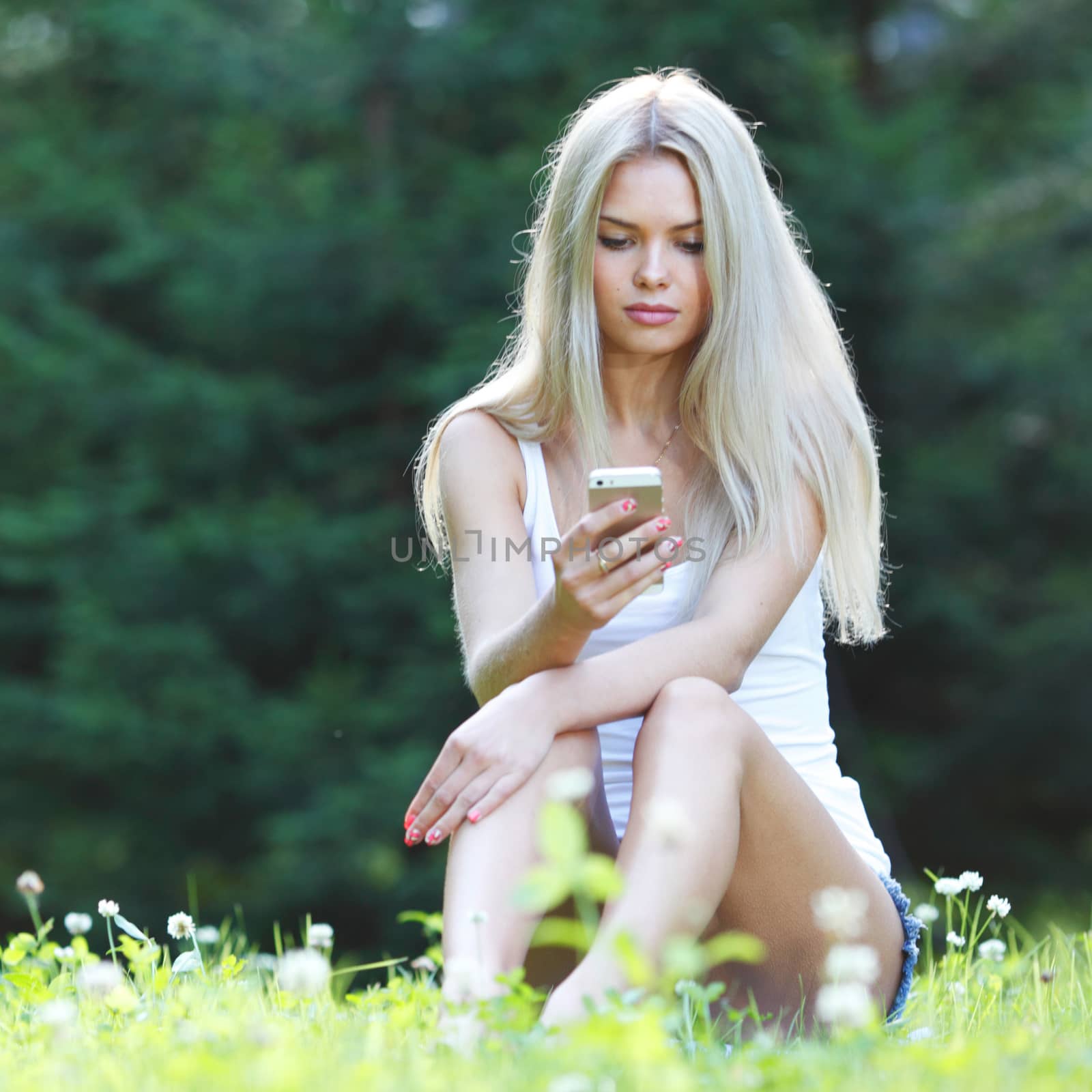 young blond woman with mobile phone sitting on grass