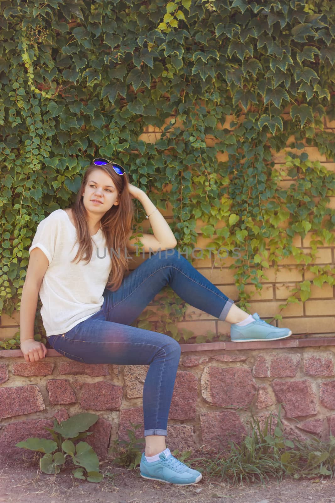 Girl sitting in the park under the wall with leaves