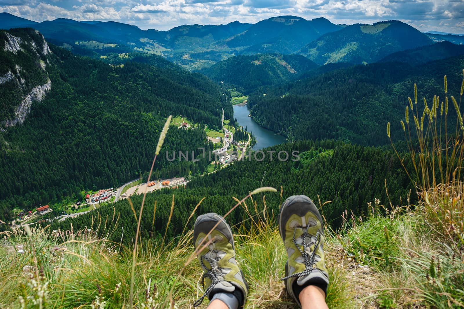 Somebody is sitting at the edge of cliff in mountains, showing his feet wearing hiking shoes. First person shoot. Retezat area, Carpathians, Romania