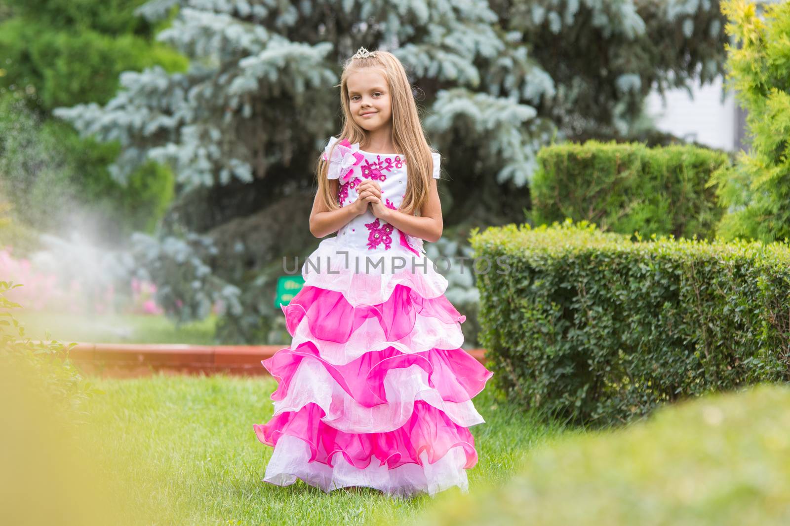 Happy six year old girl in a lush evening pink dress walking through the green garden