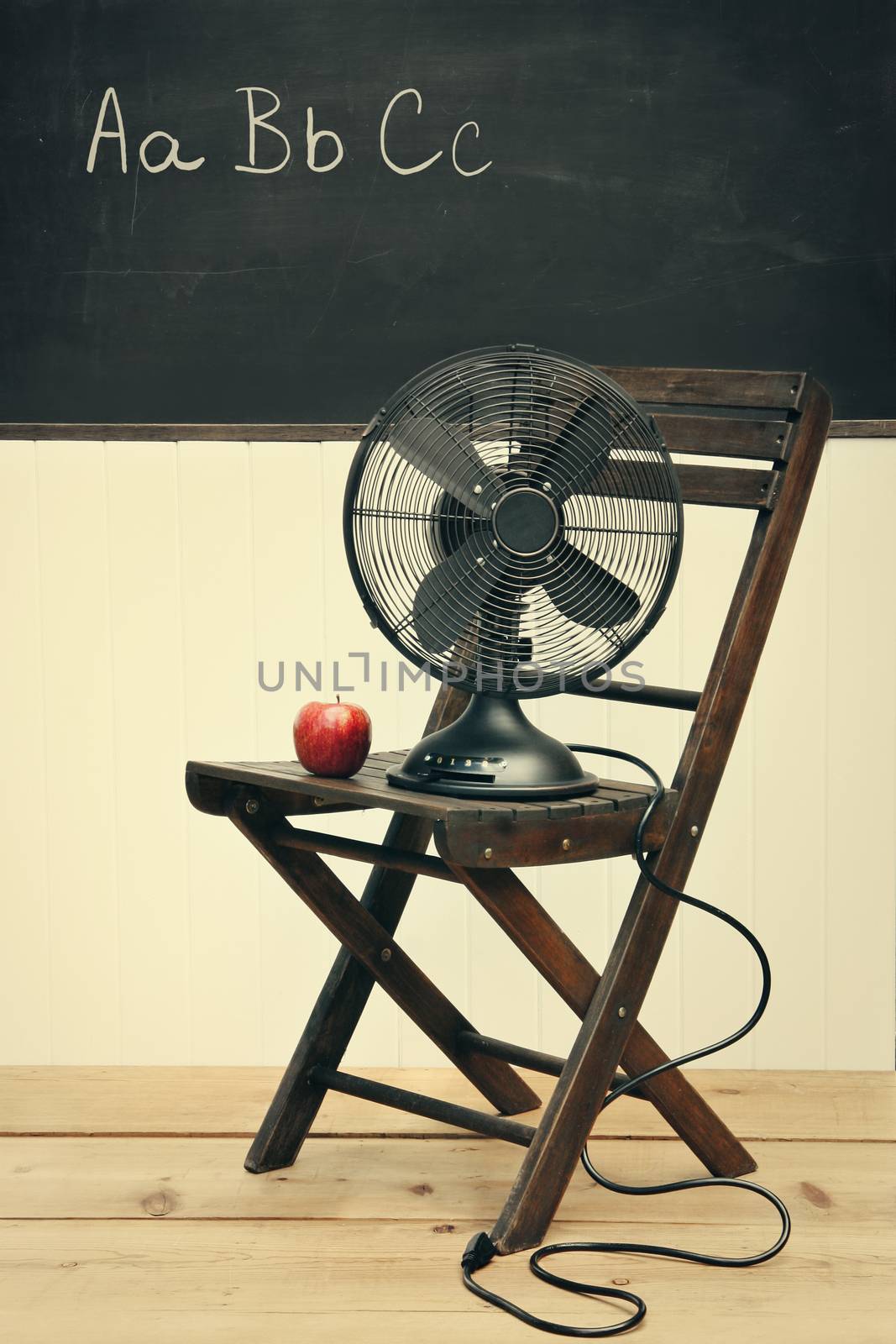 Old fan with apple on chair in school room by Sandralise