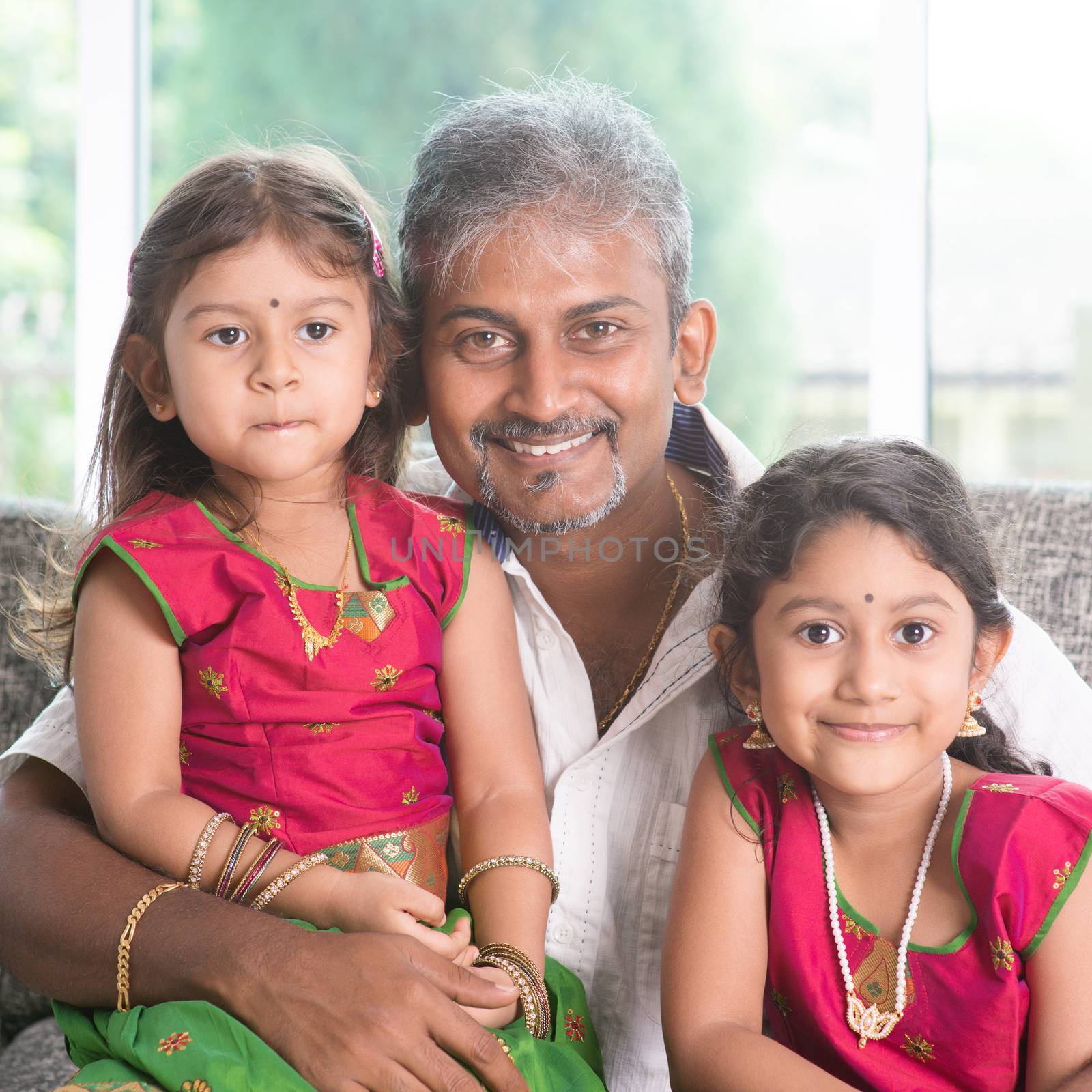 Happy Indian family at home. Asian father and daughters sitting on sofa smiling. Parent and children indoor lifestyle.