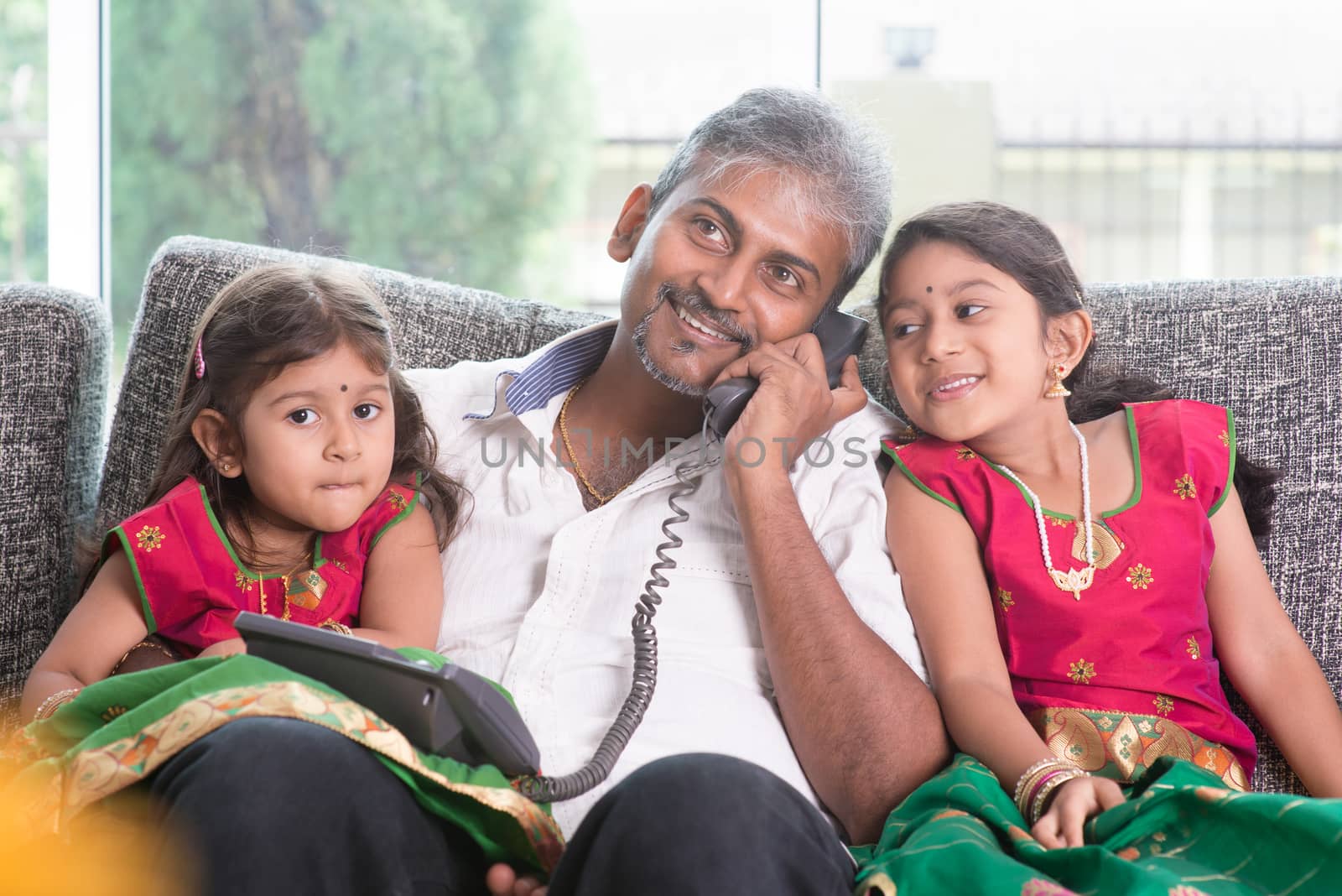 Husband making a phone call to wife while taking care of children at home. Asian Indian family at home.