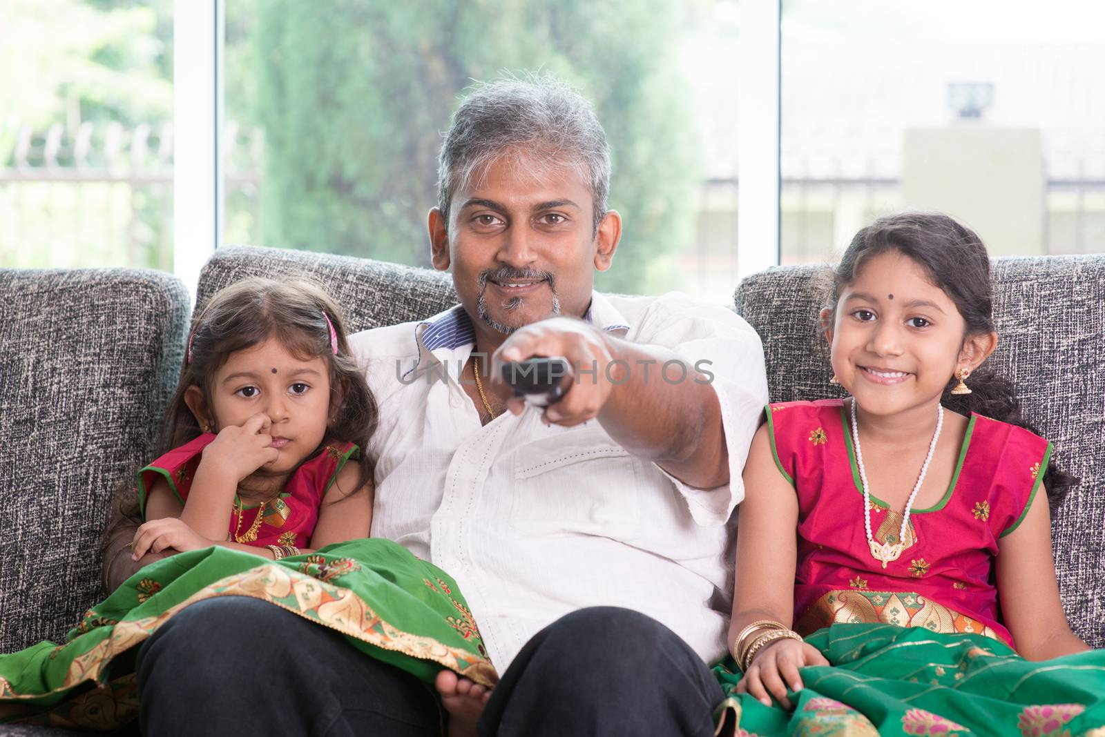 Happy Indian family watching tv together, father and children indoor living lifestyle at home.
