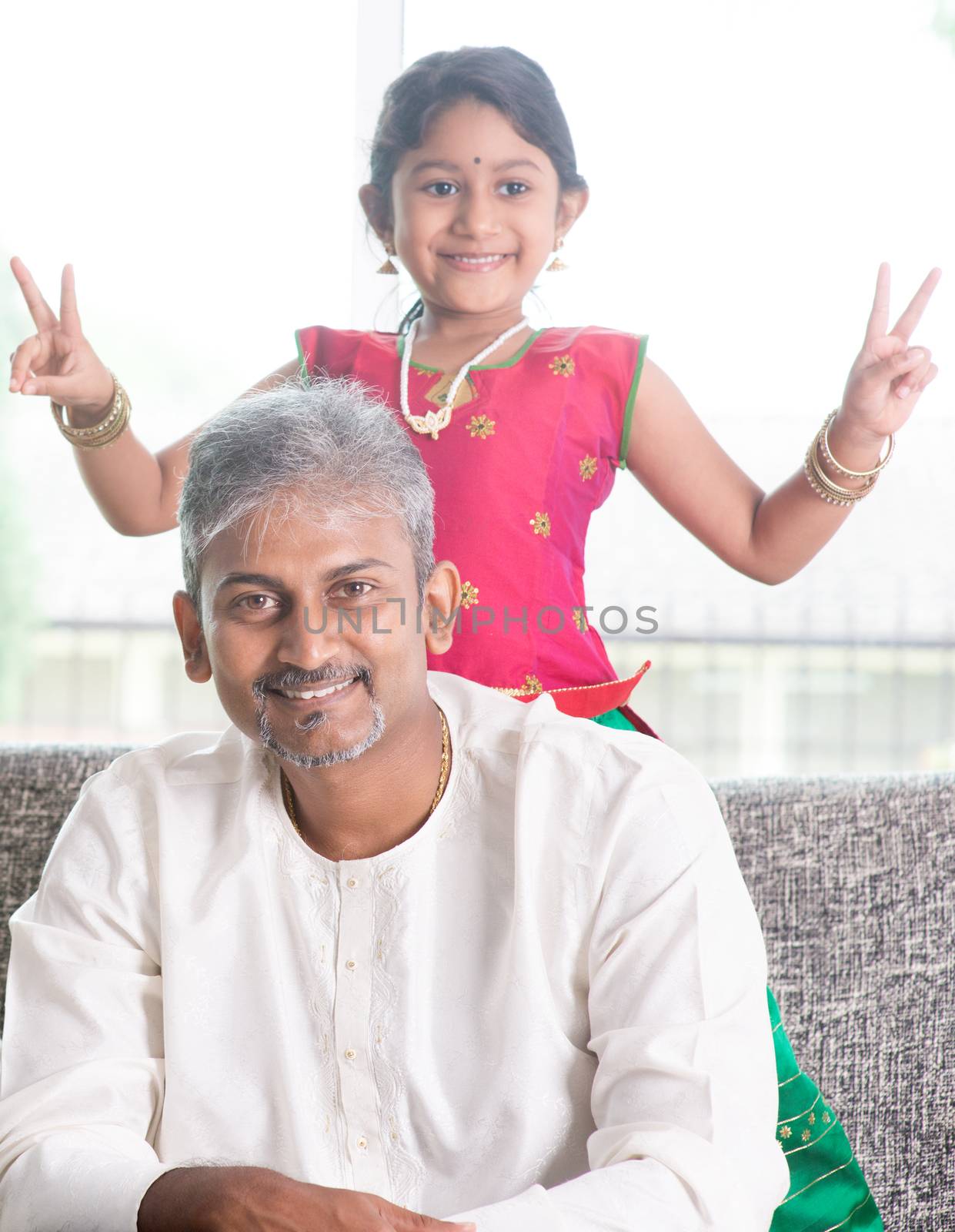 Happy Indian family at home. Asian girl showing peace hand sign. Adults and kids indoor lifestyle.