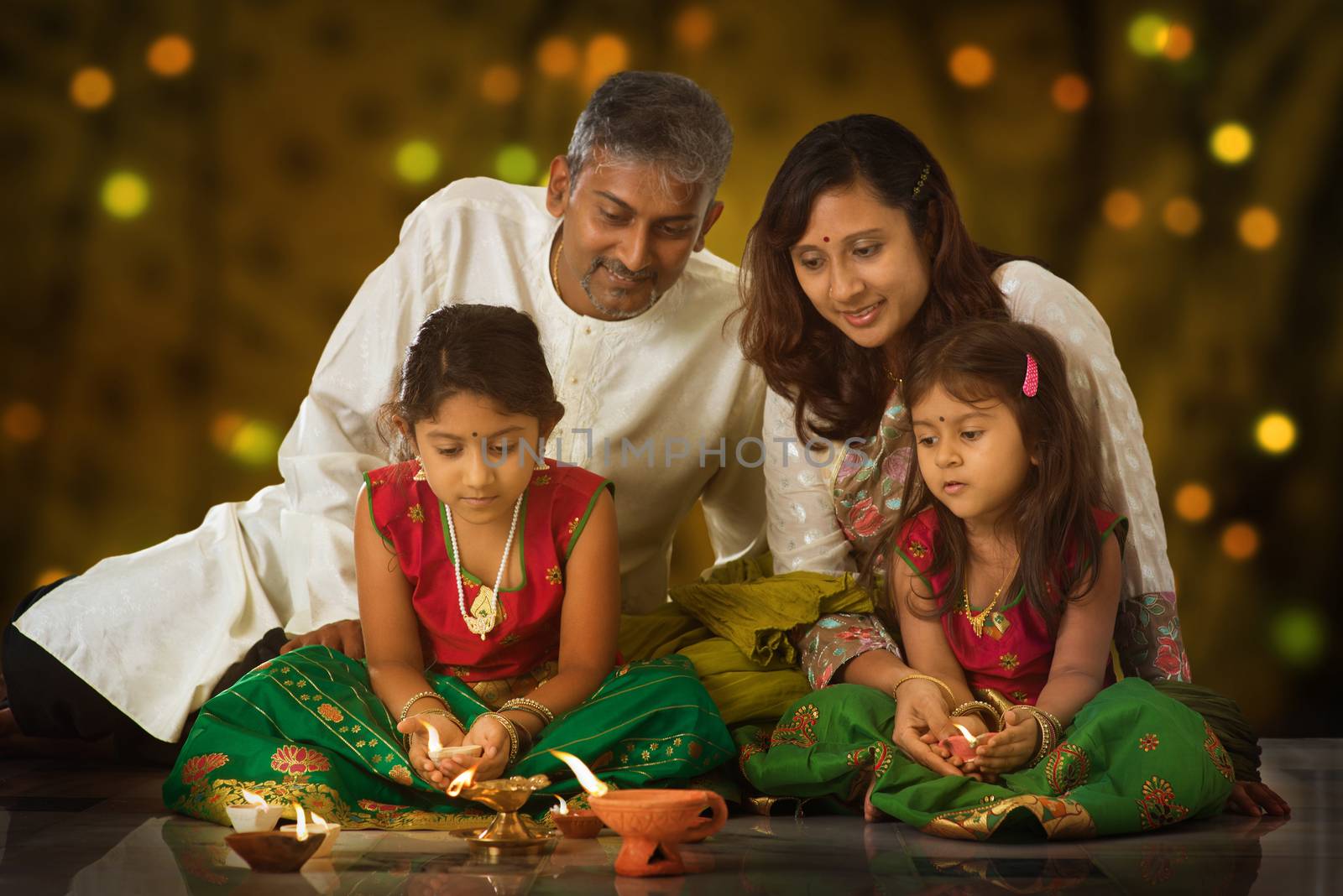 Indian family in traditional sari lighting oil lamp and celebrating Diwali, fesitval of lights inside a temple. Little girl hands holding oil lamp indoors.