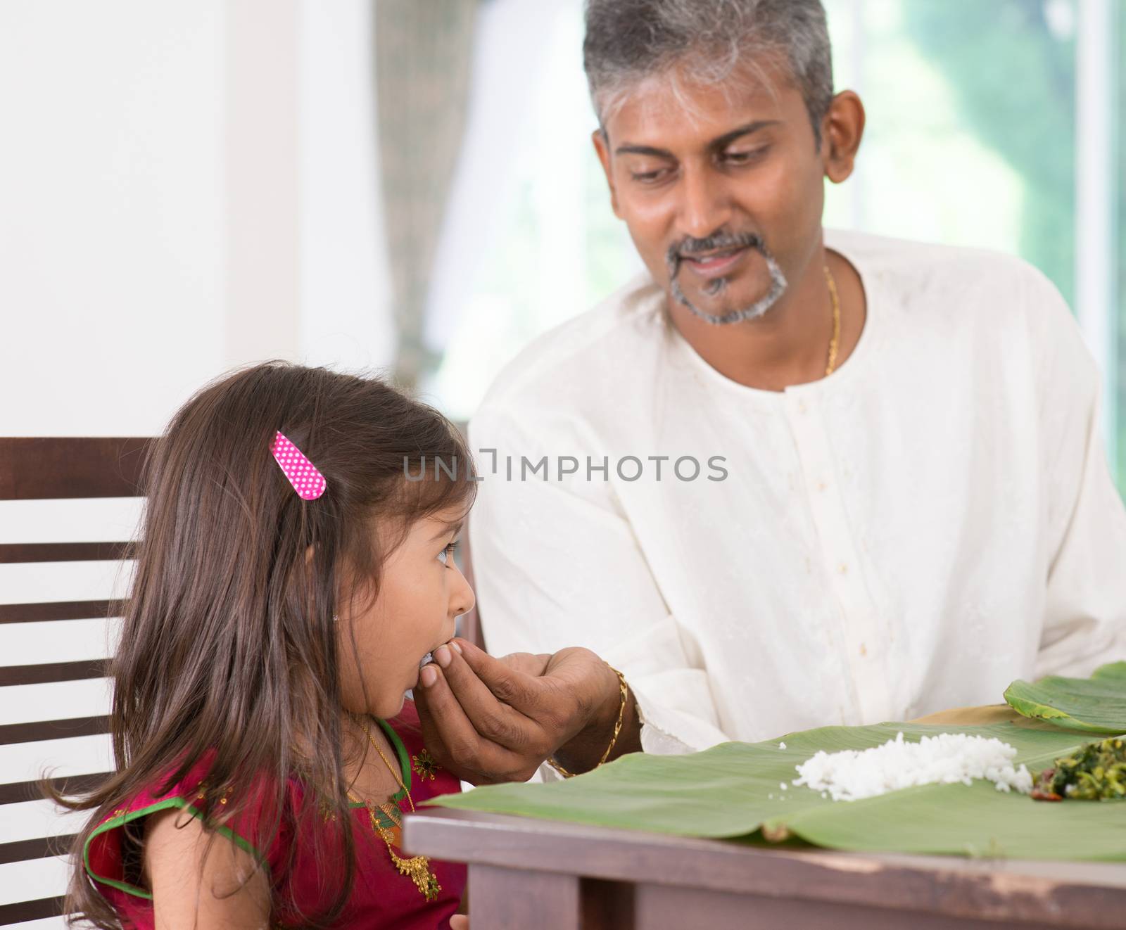 Indian family dining at home. Candid photo of India people eating rice with hands. Parent feeding child.