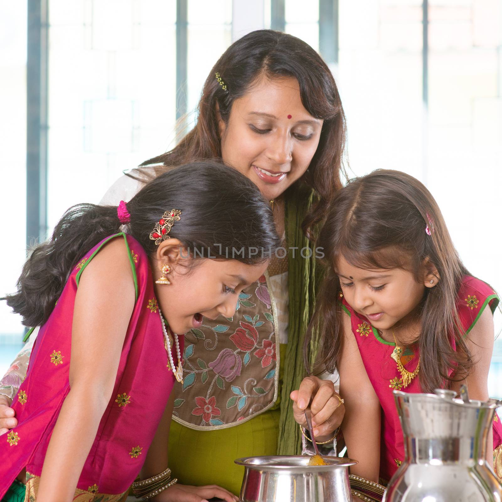 Asian family cooking food together in kitchen. Indian mother and children preparing meal at home. Traditional India people with sari clothing.