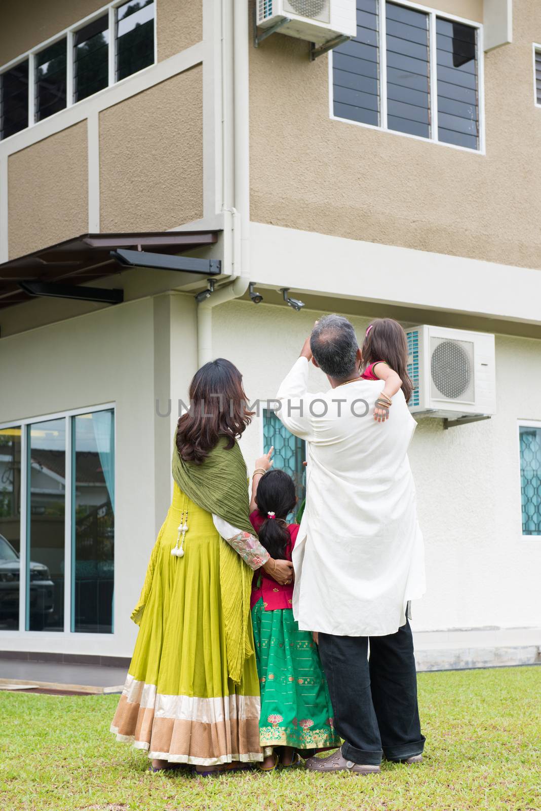 Rear view of Indian family in traditional dress saree standing outdoors and pointing to their new home.