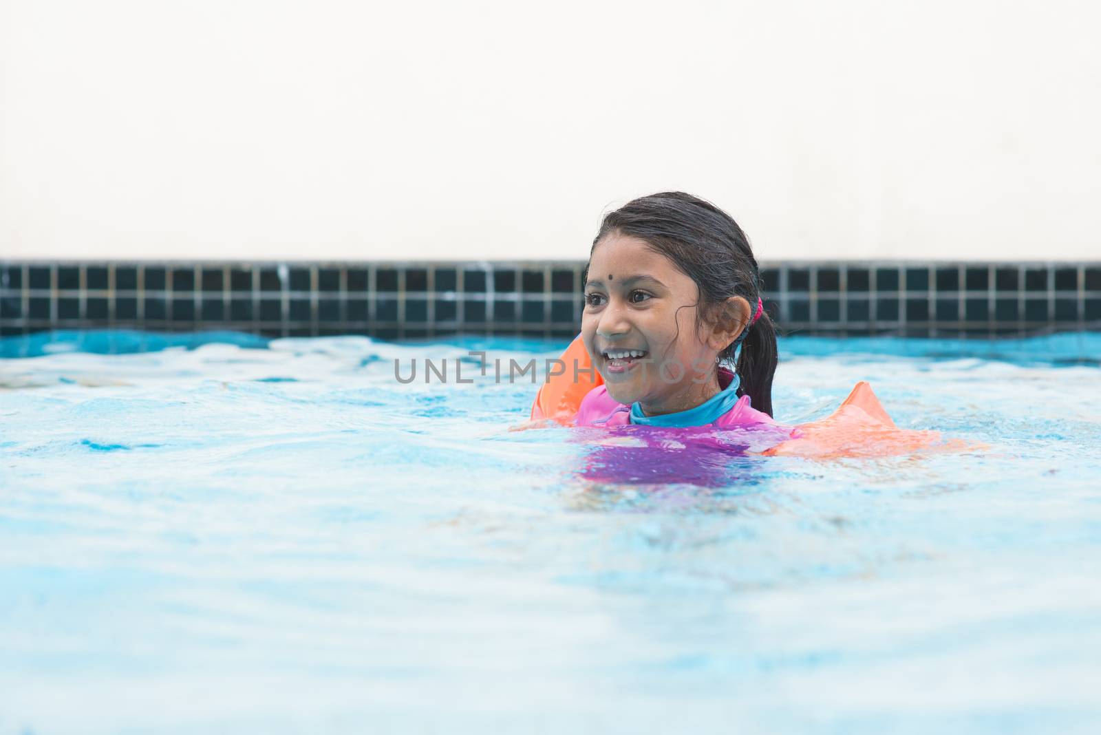 Asian girl in swimmer class with float bands. Indian child learning swimming in pool.
