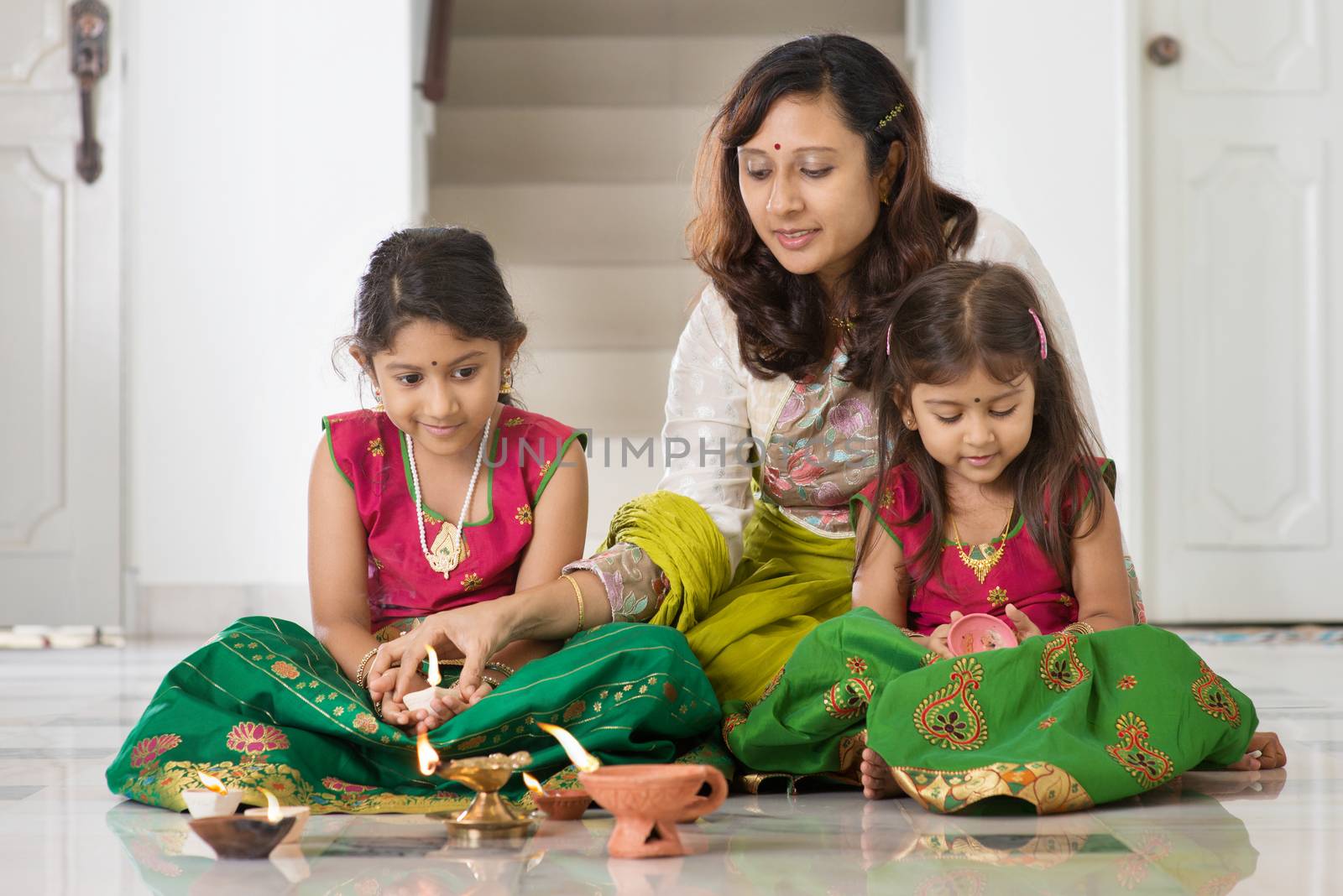 Indian family in traditional sari lighting oil lamp and celebrating Diwali, fesitval of lights at home. 