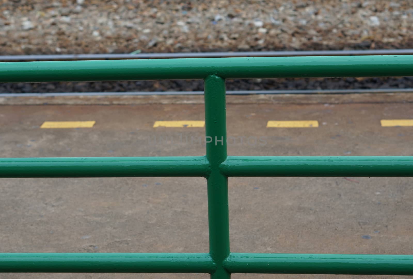 Green metal fence and yellow dash line at train station.                      
