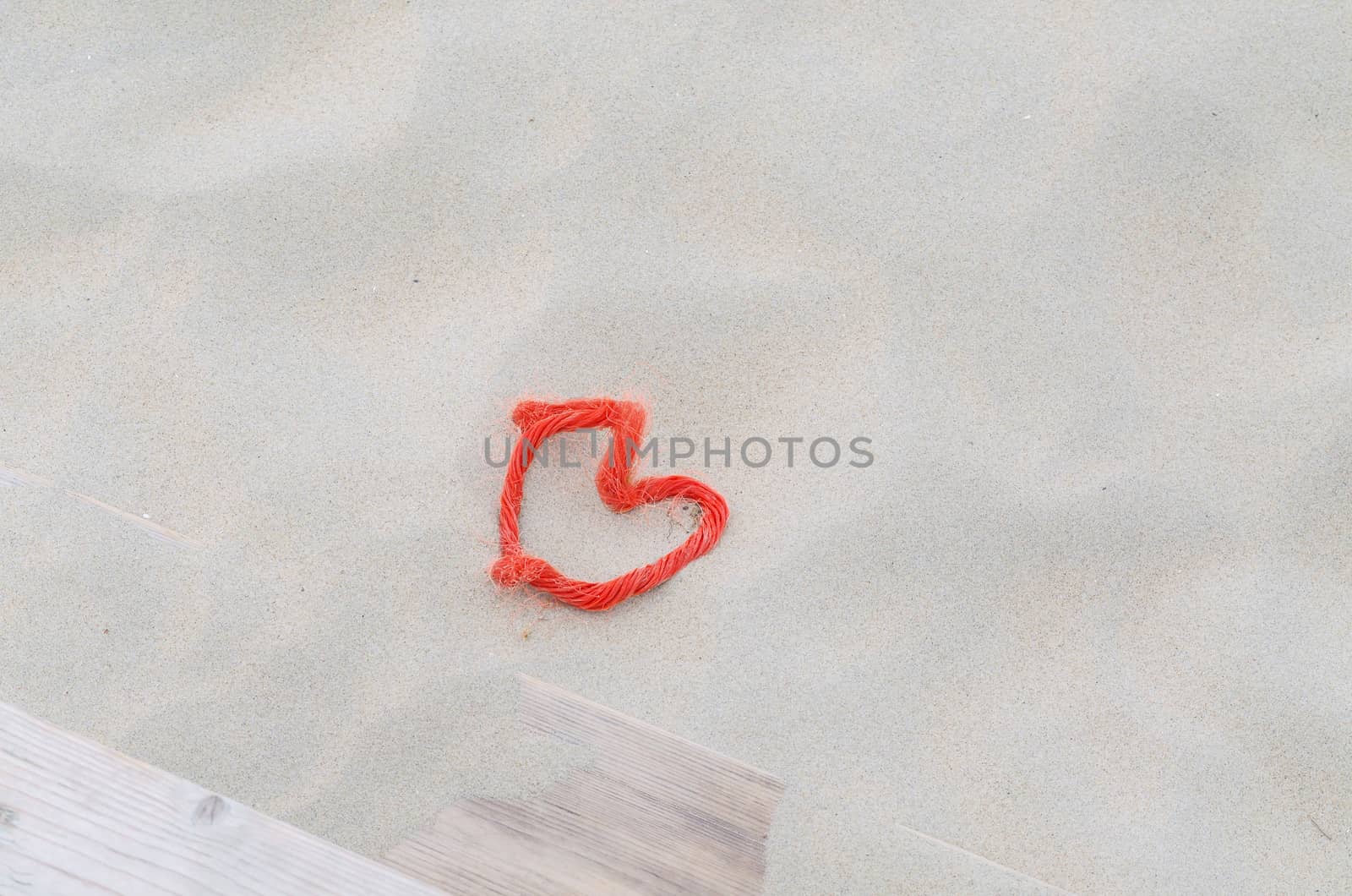 A red rope in heart shape lying in the sand. Beach background. Top View