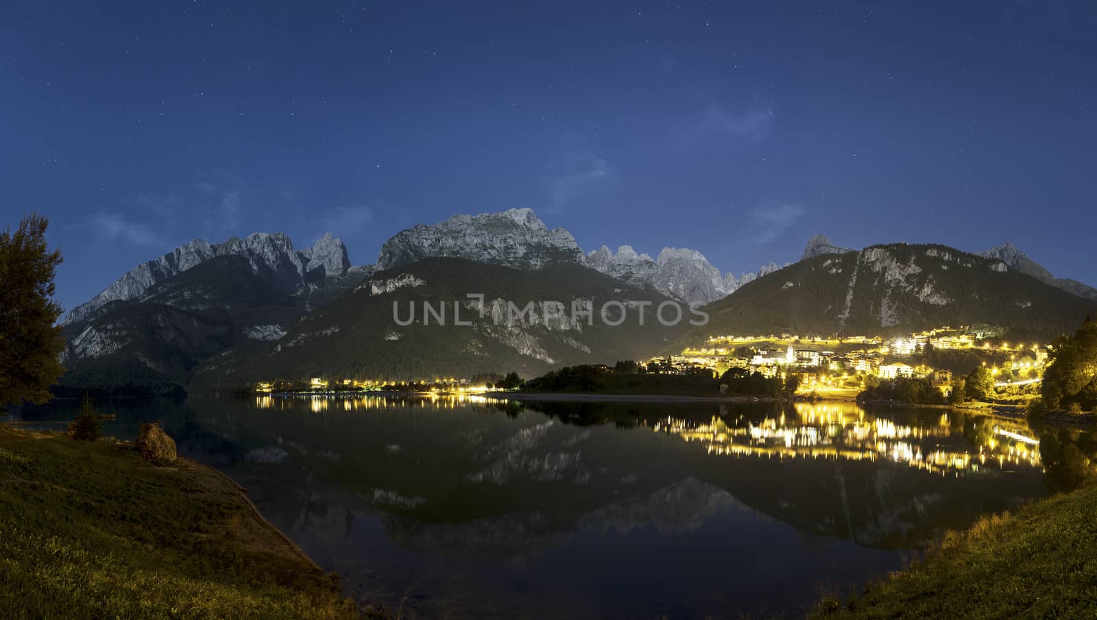 Night landscape on the Moveno lake and city with Dolomiti of Brenta Group in background at the moonlight