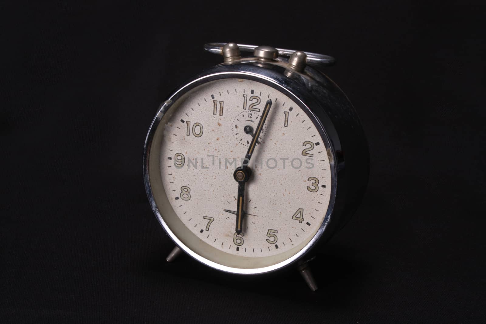 A vintage alarm clock with a white dial, on black studio background.