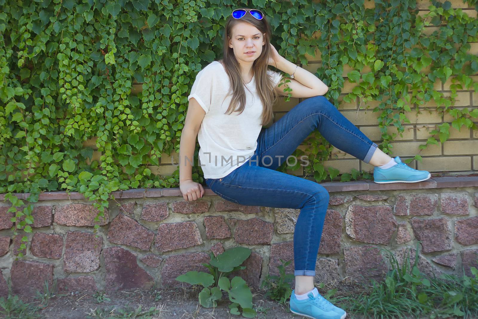 Girl in jeans sits near the fence with thickets