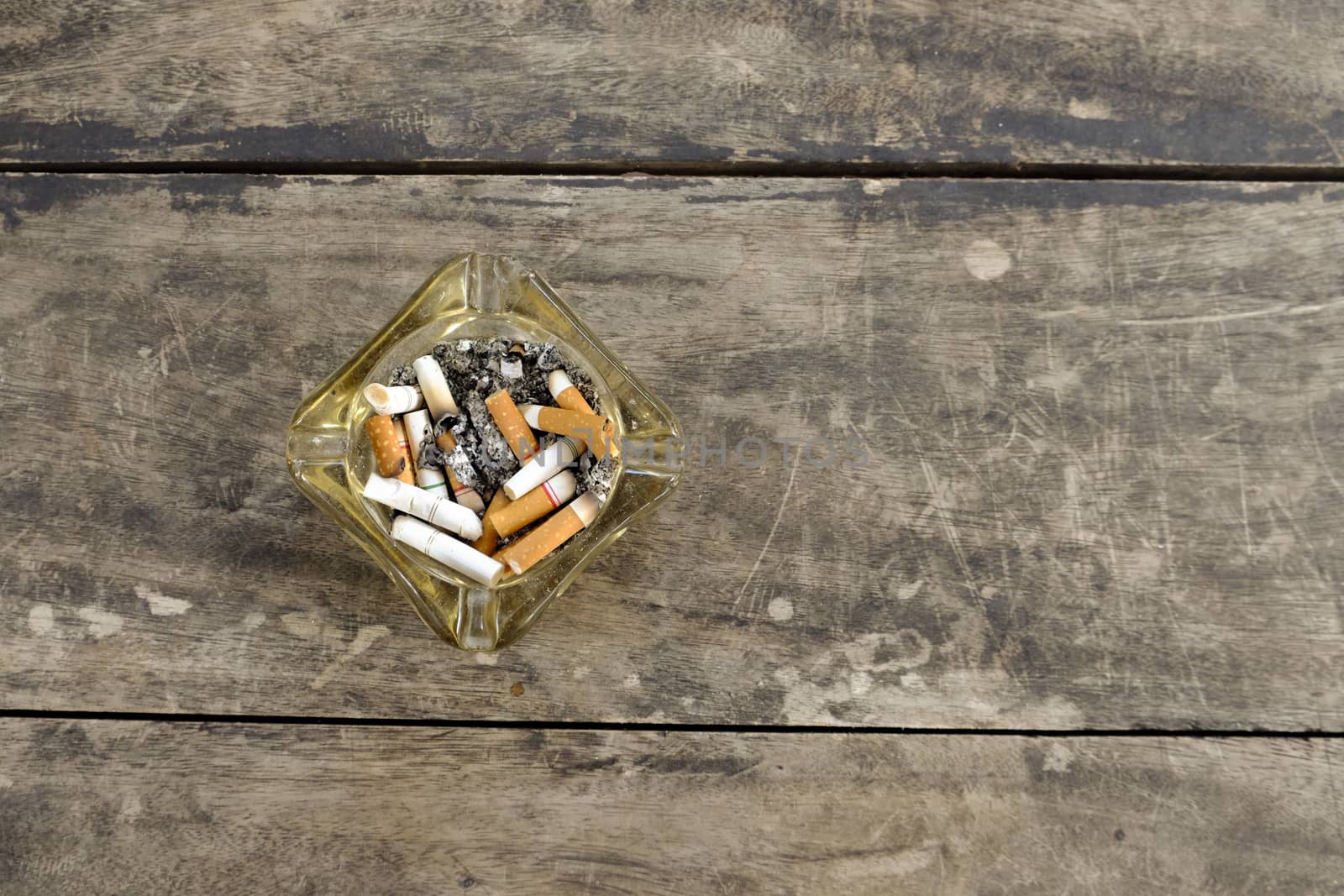 ashtray full of butt cigarettes on wooden background