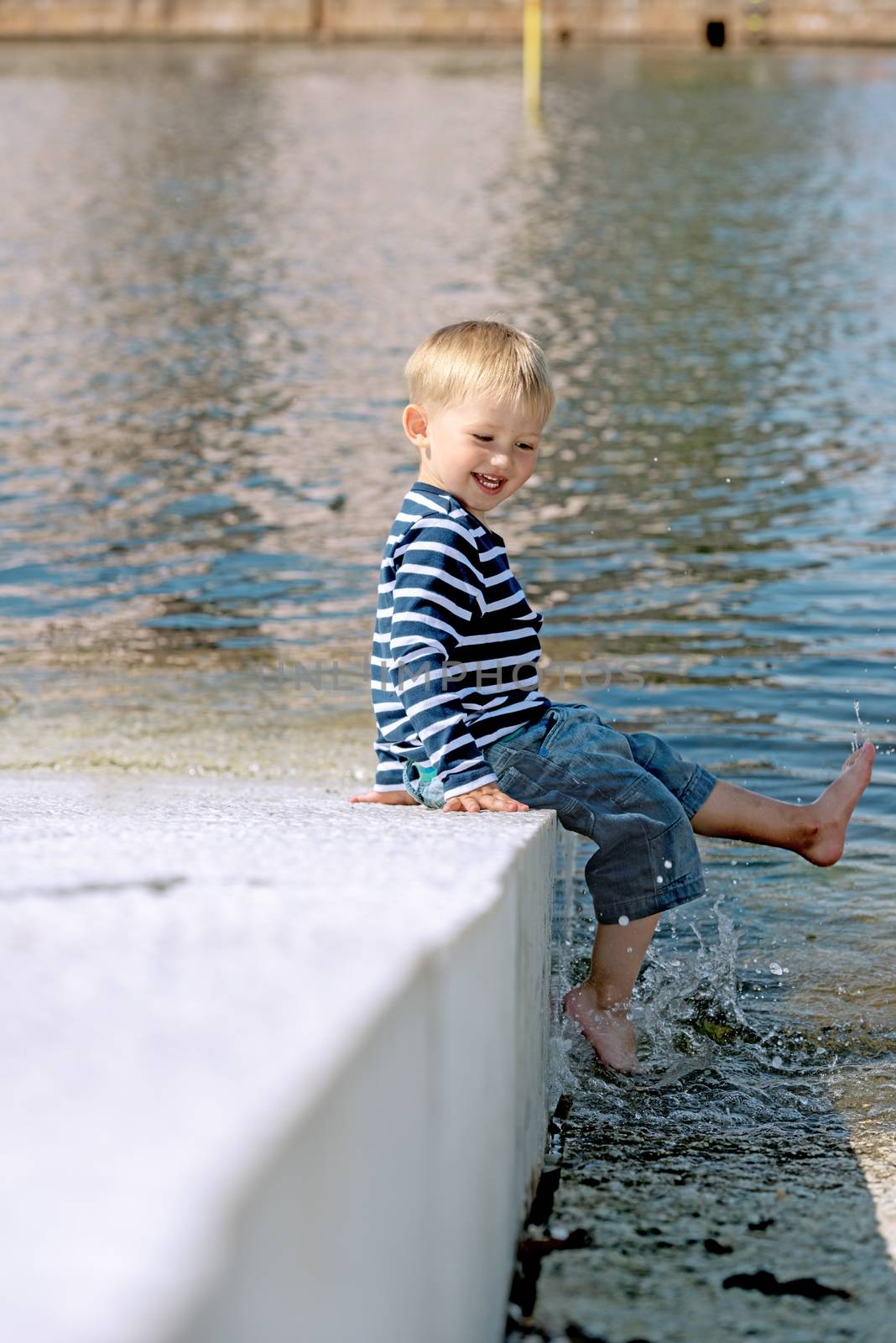 Little preschool boy playing outdoors near water by Nanisimova