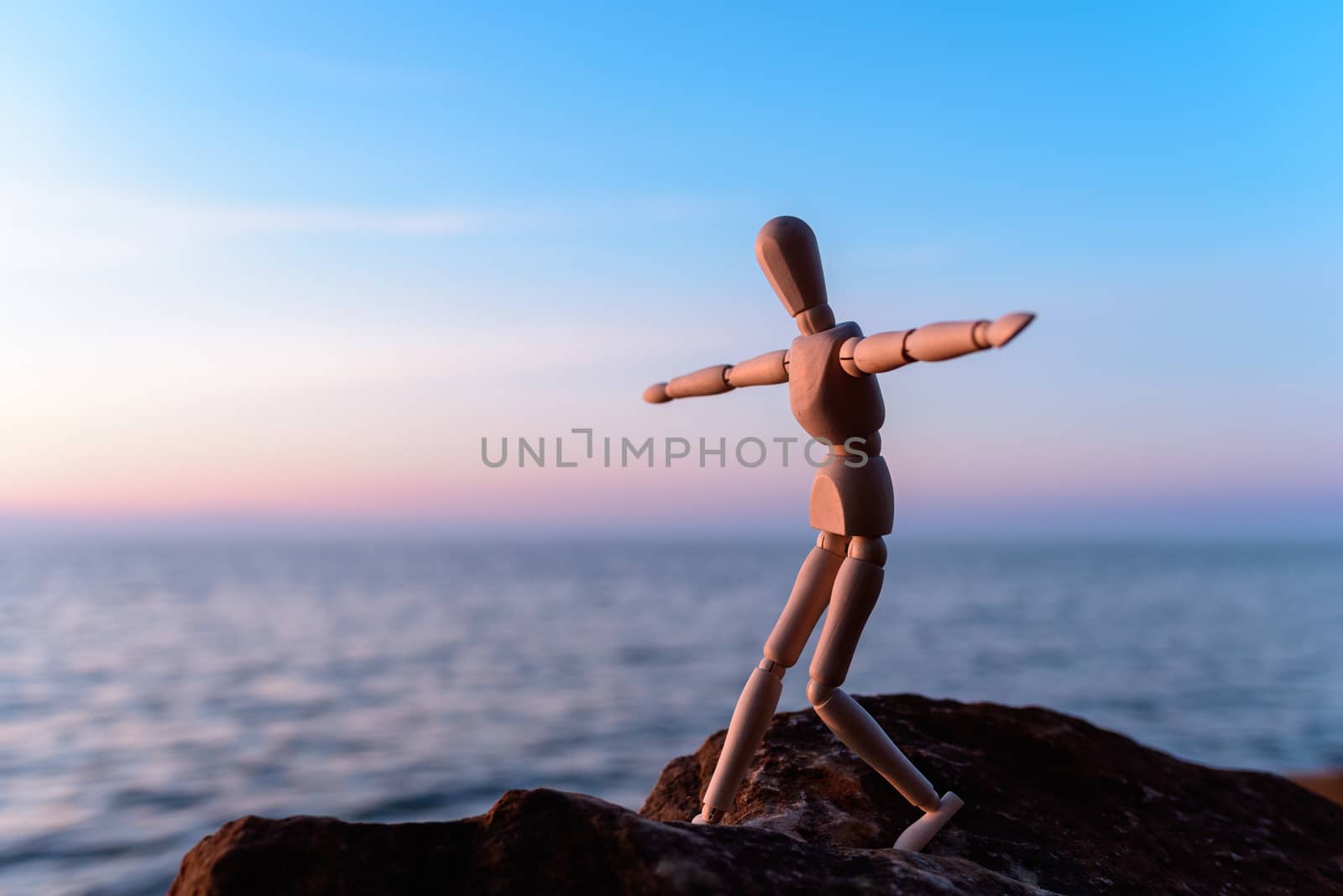 Wooden man stands on the top of sea boulder