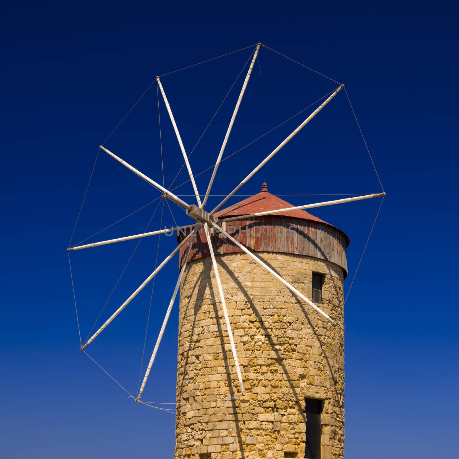 Stone Windmill stand against the blue sky at Mandraki Harbour, Rhodes