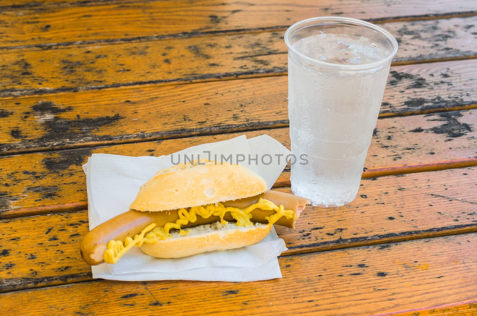 Sausage with mustard on buns. The sausage is on a brown wooden table.