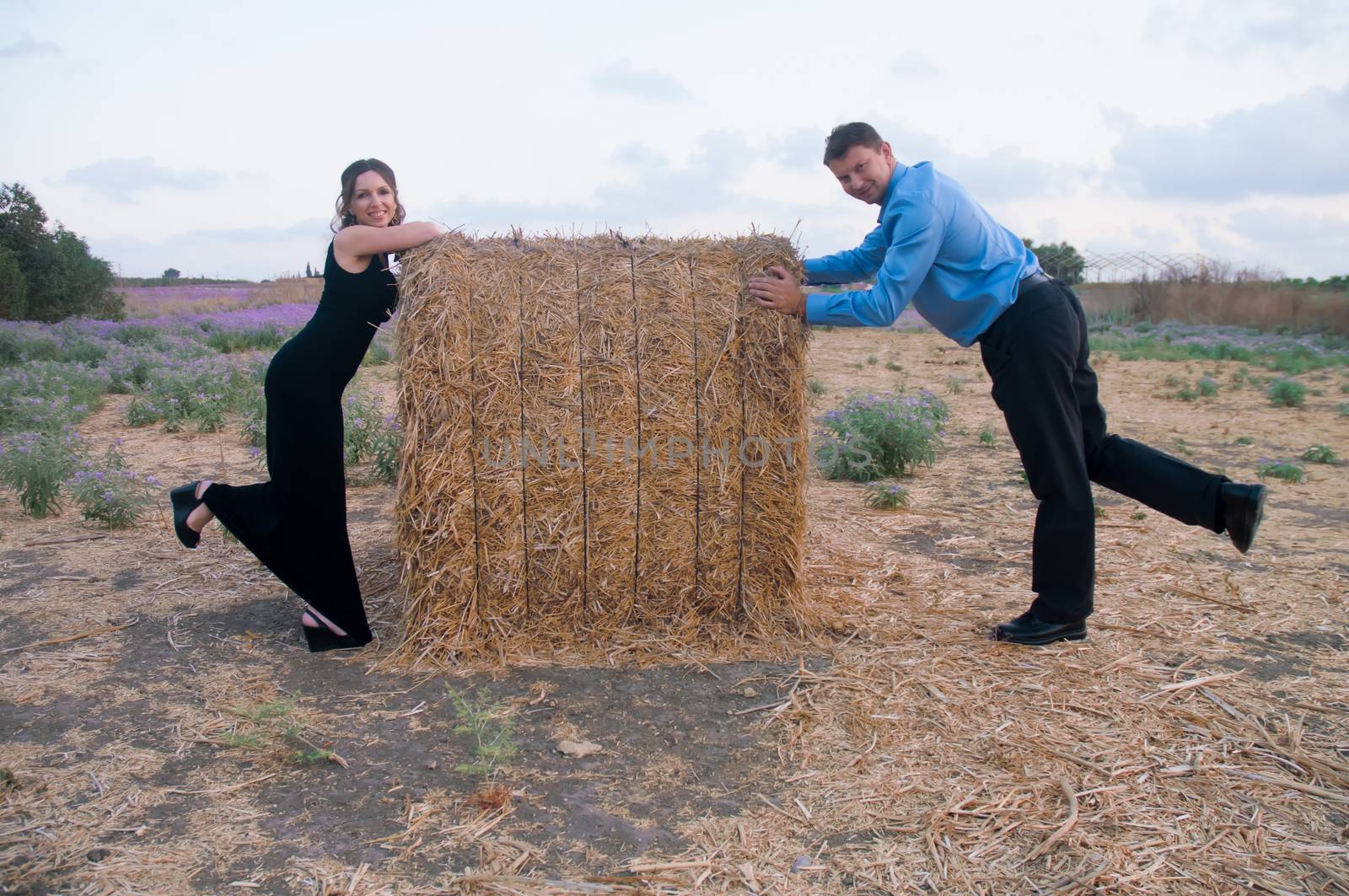 Elegant young couple on a romantic walk in a field of blossoming lavender and oblique hay.