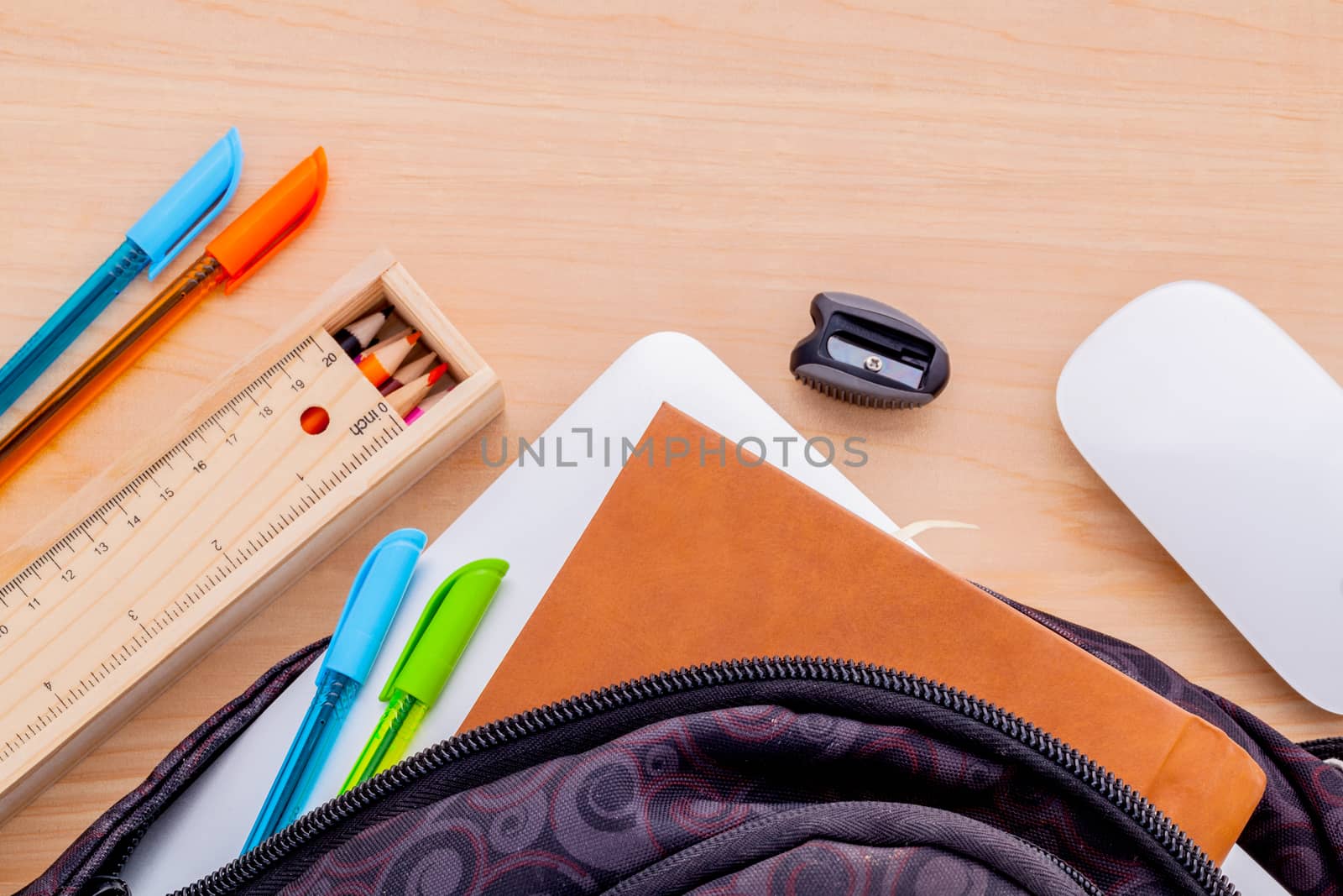 Backpack with school supplies laptop,book stationary,mouse,pen,ruler, and color pencil on wooden table .