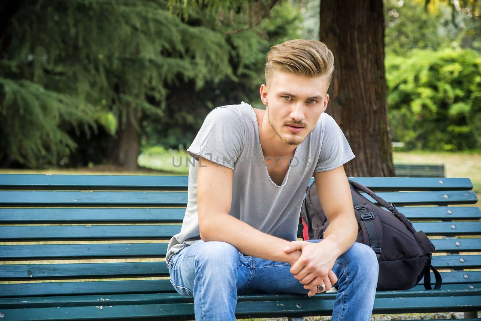 Handsome blond young man sitting on park bench by artofphoto