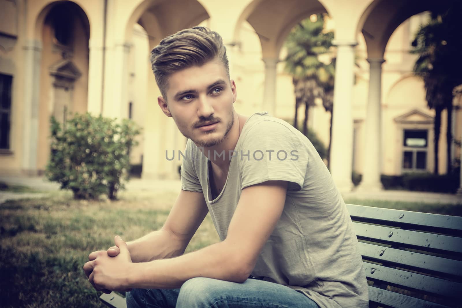 Handsome blond young man sitting on park bench by artofphoto