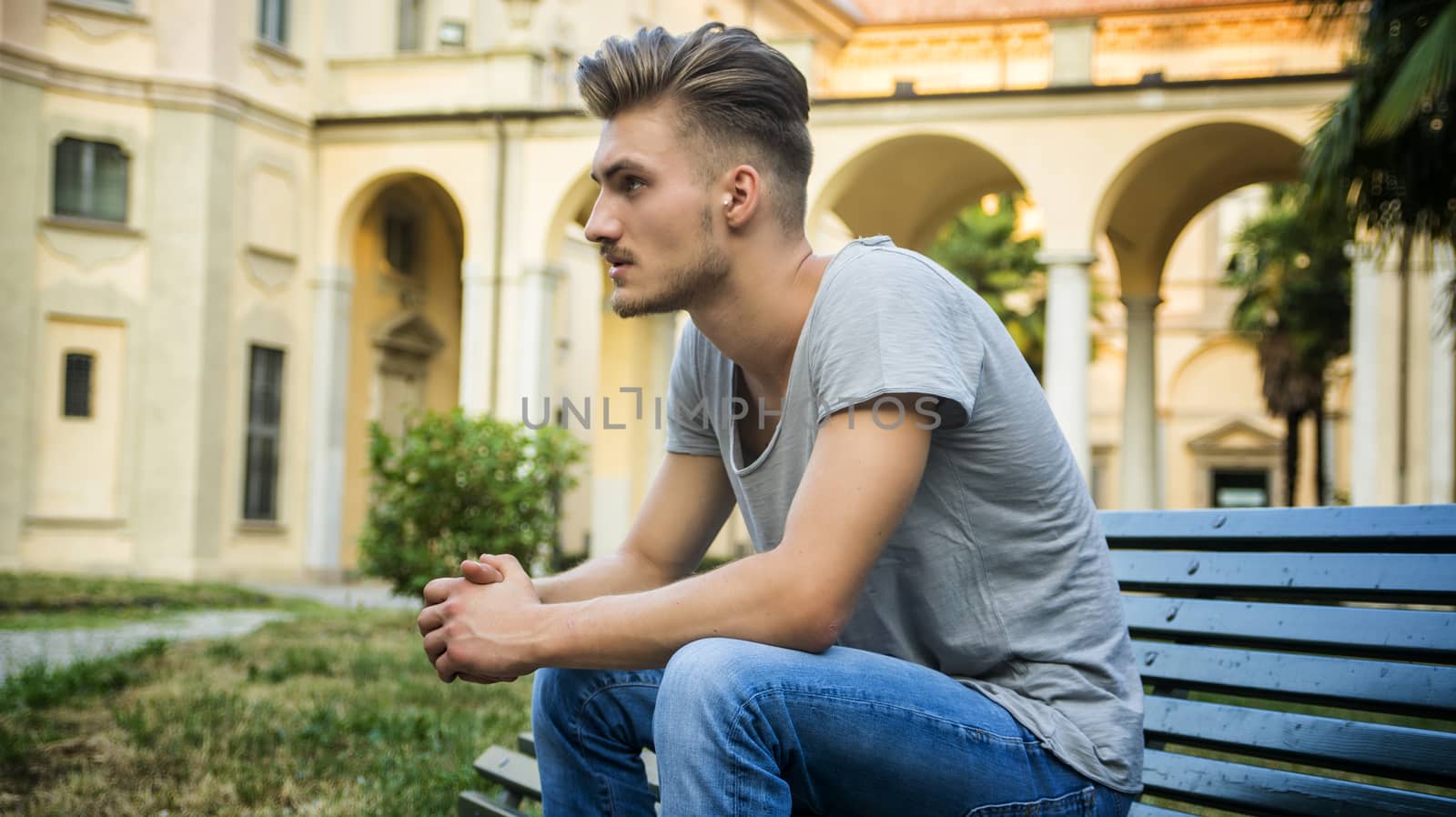 Handsome blond young man sitting on green, wooden park bench