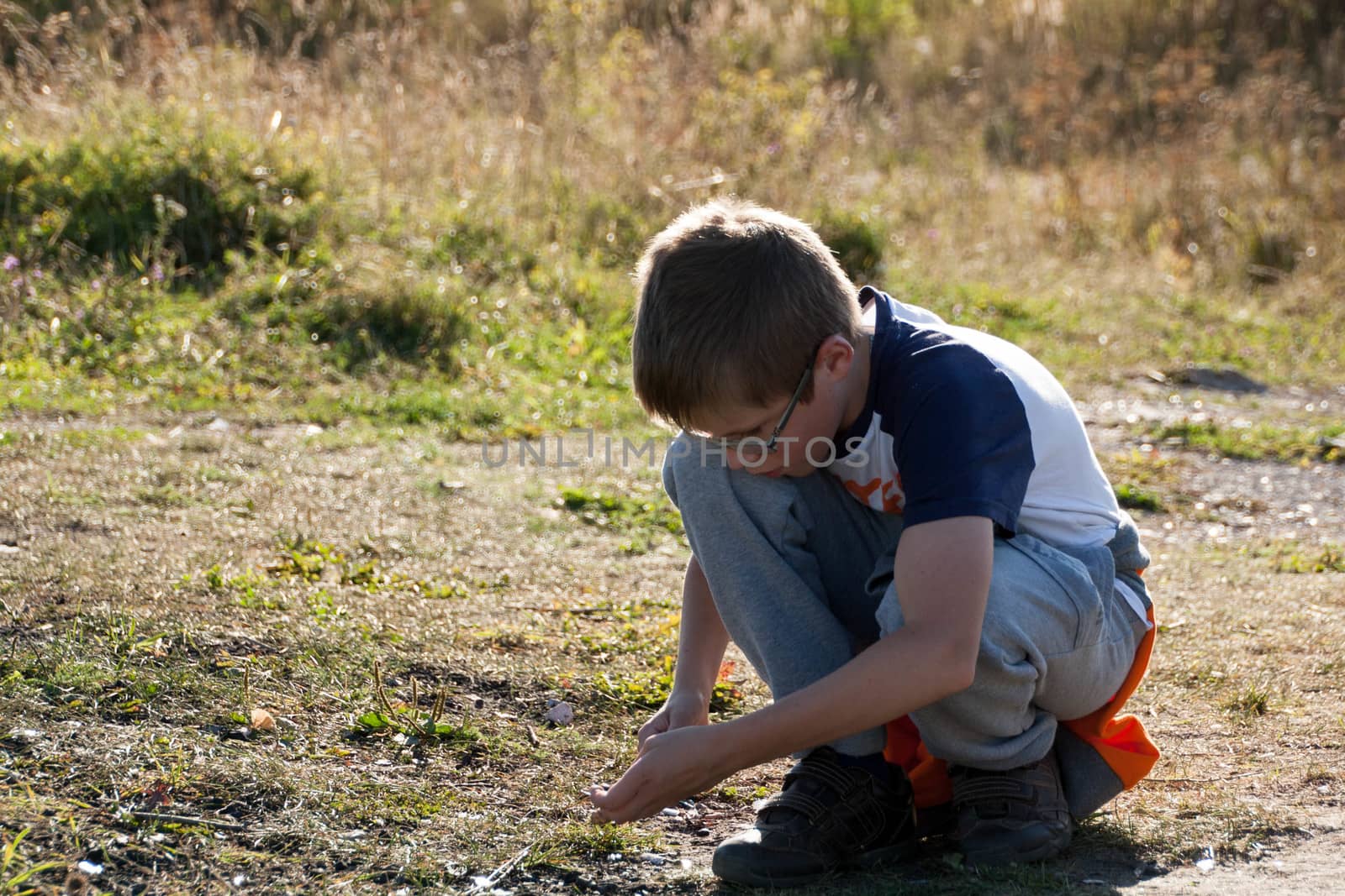 a boy sits in a field and looking for the stone