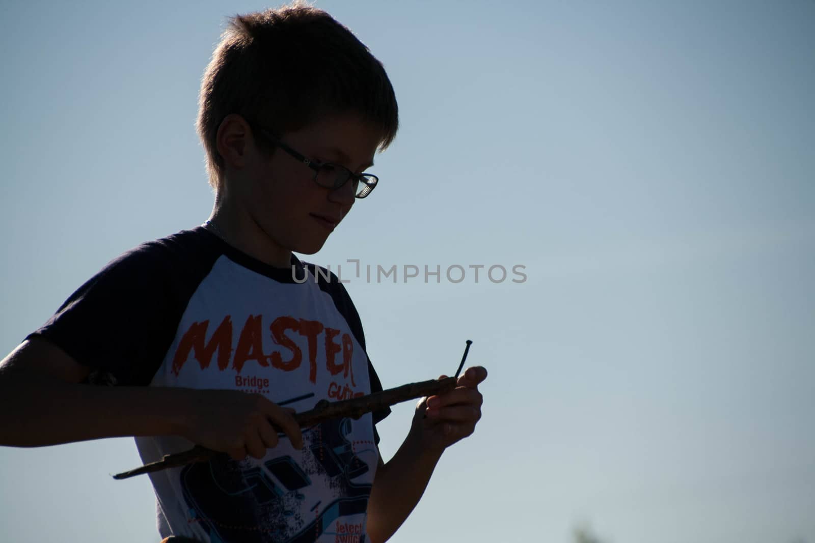  boy stands in a field with a stick on blue sky background