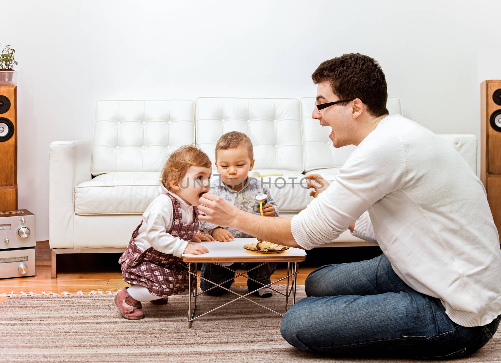 A young father feeding two little children - a boy and a girl at home.