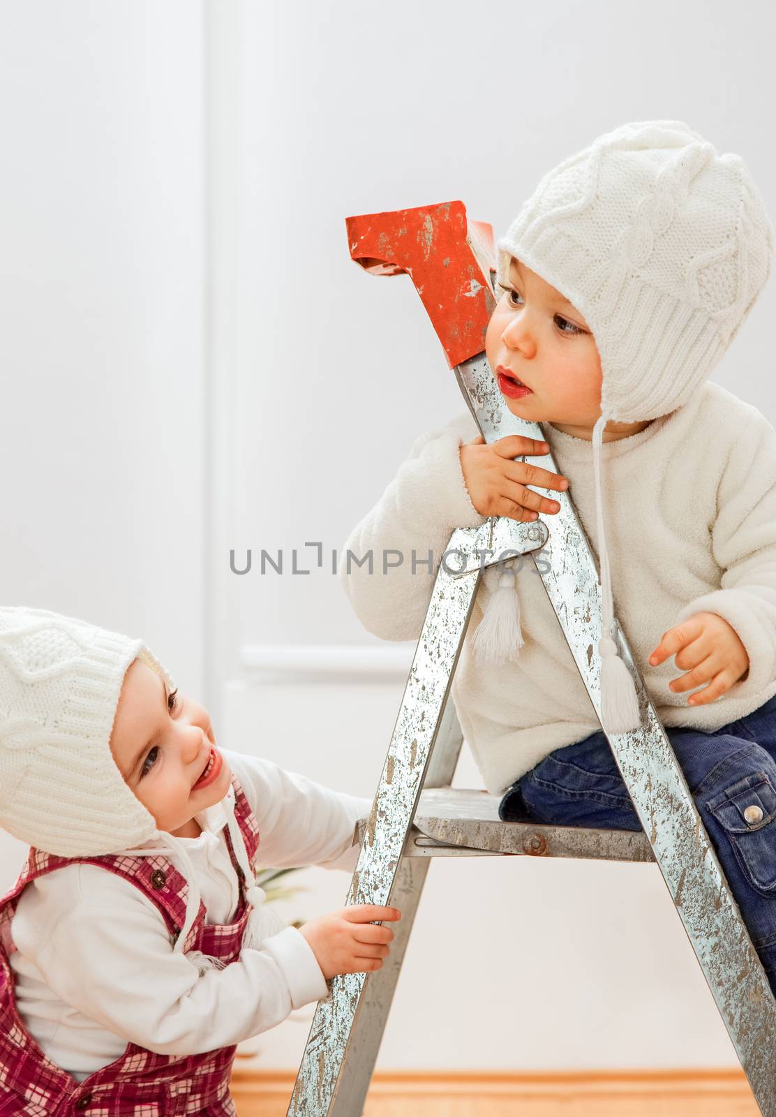 Two litlle kids playing on a ladder in a room of a new apartment.