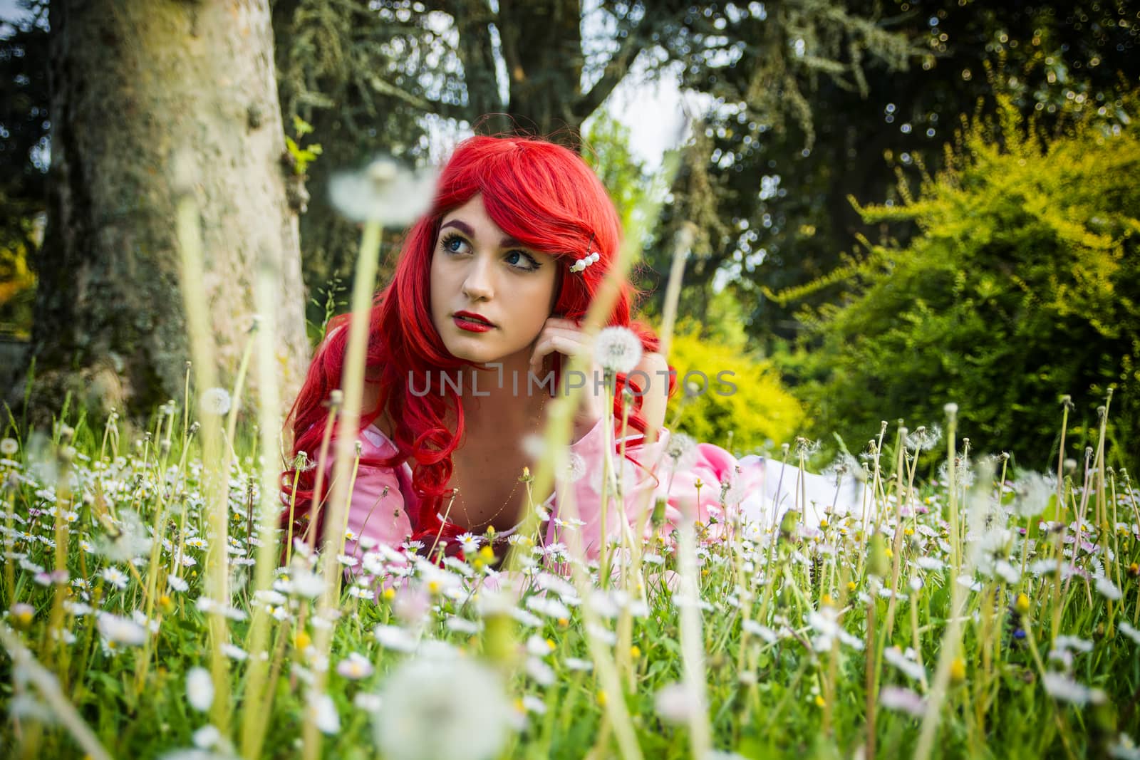 Young Woman with Bright Red Hair Lying Down in Forest Flower Field with Hand Resting on Chin Looking Dreamily Off Into Space