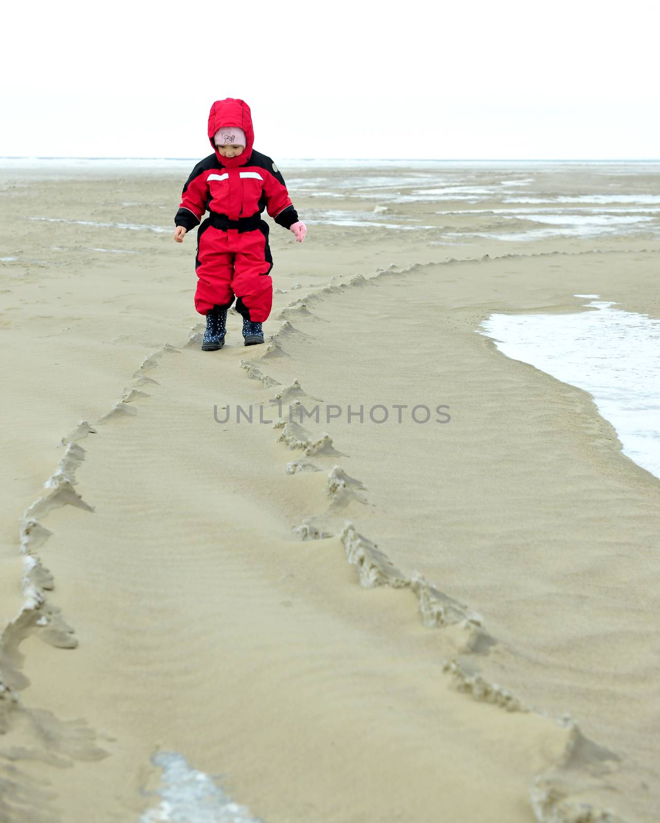 The little girl goes on the sandy coast in winter clothes